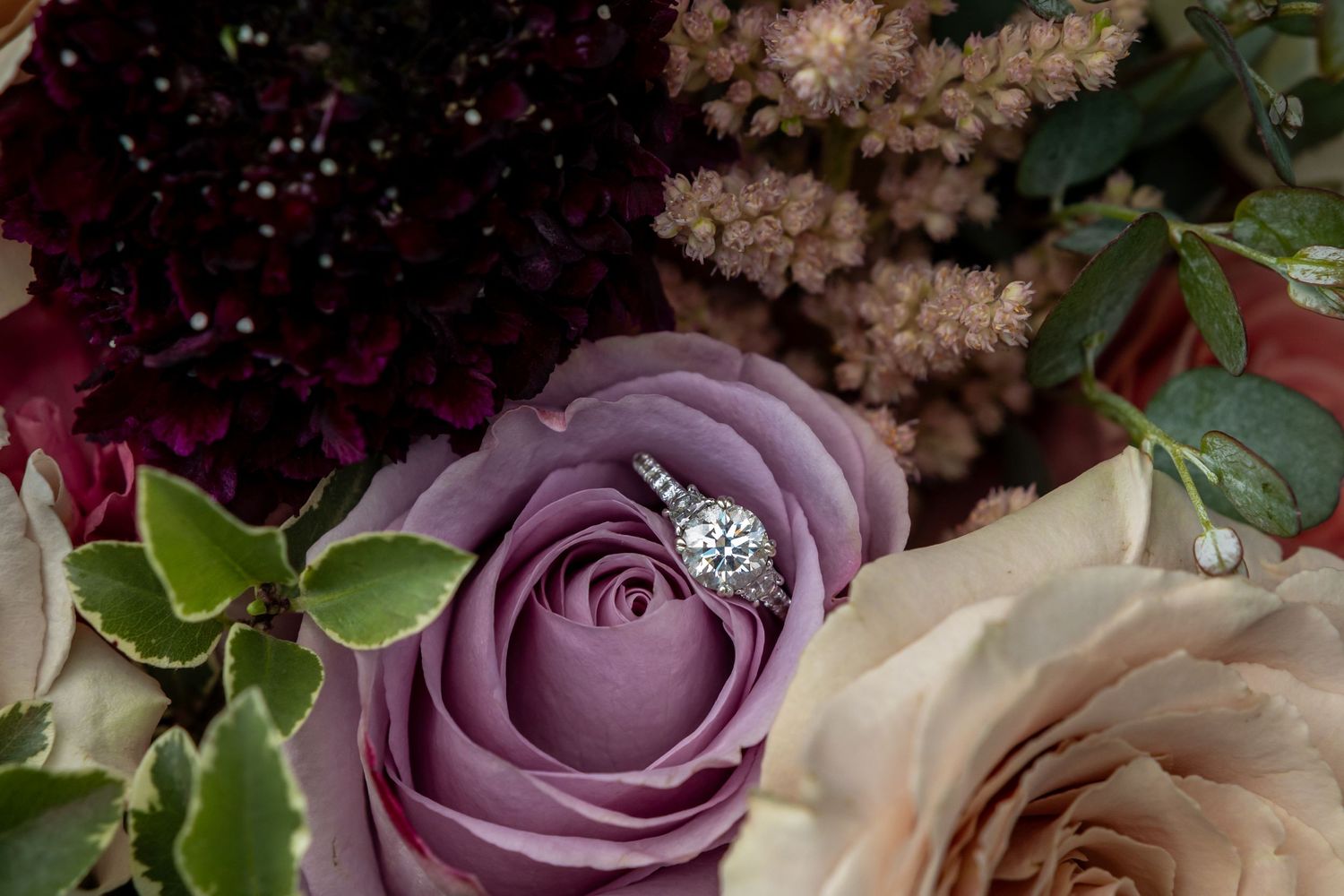 A romantic bouquet of purple and white roses with delicate greenery arranged for a wedding.