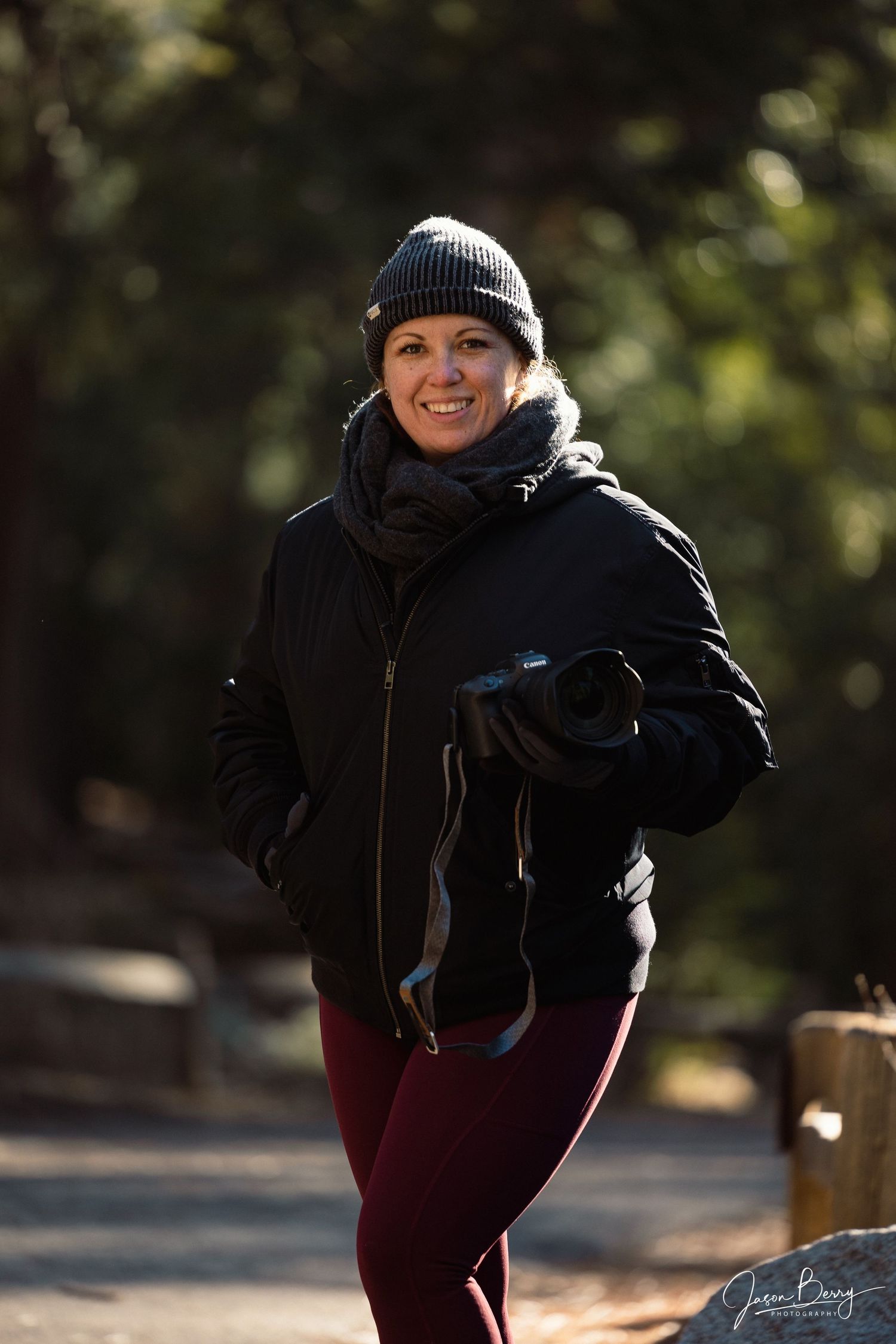 Person bundled up in winter clothing and beanie hat posing outdoors on a sunny day.
