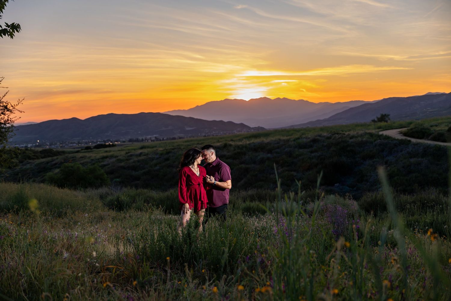 Silhouetted couple watching sunset over mountain landscape.