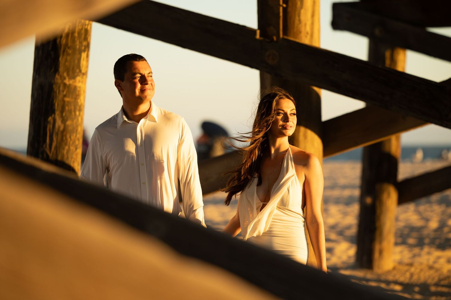 Silhouetted figures embrace during sunset under wooden beams at a scenic overlook.