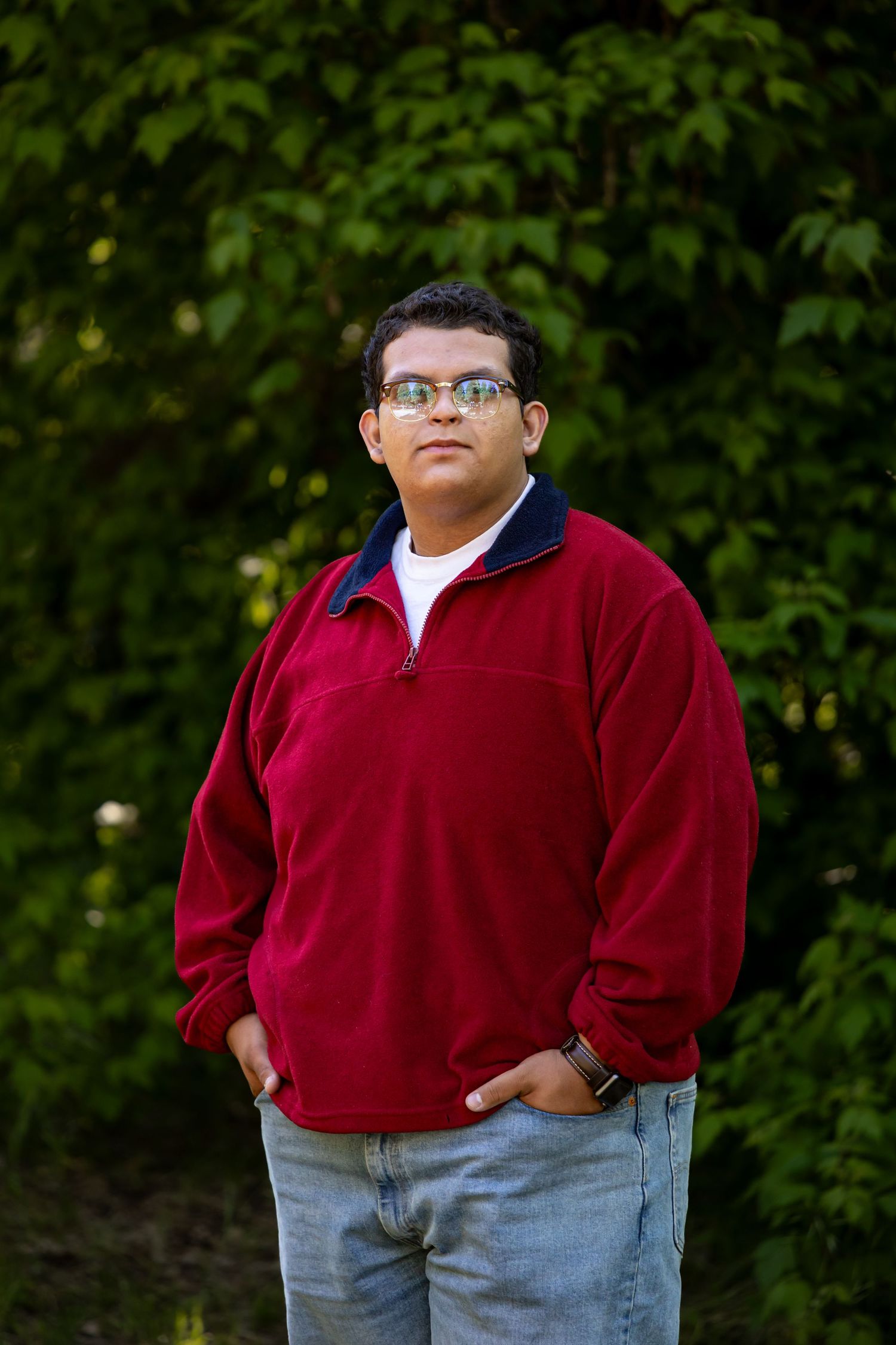 A casual portrait in a red fleece pullover and jeans standing against lush green foliage in Yucaipa.