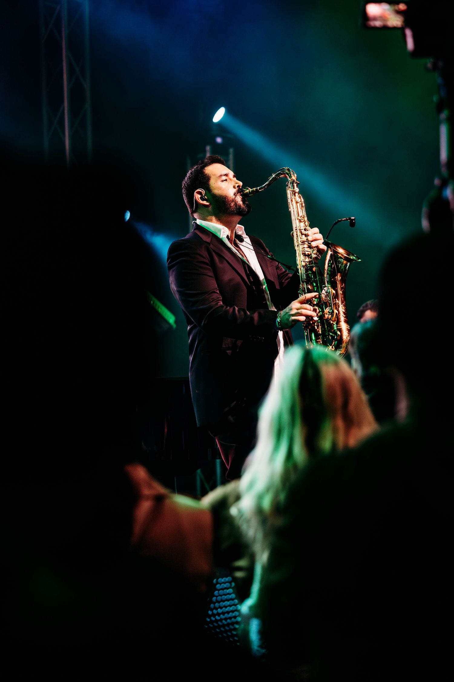 Saxophonist in formal attire performs solo under dramatic spotlight with crowd in foreground in Garden Grove.