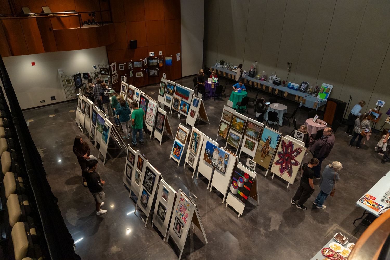 An art gallery exhibition displays multiple framed works on dark walls with spotlighting.