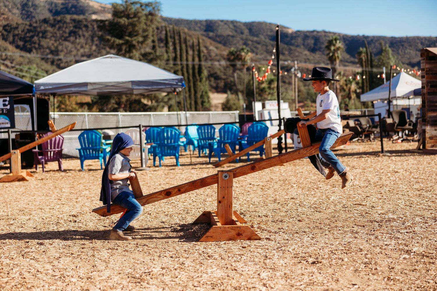 Two people playing on a seesaw at an outdoor country festival.