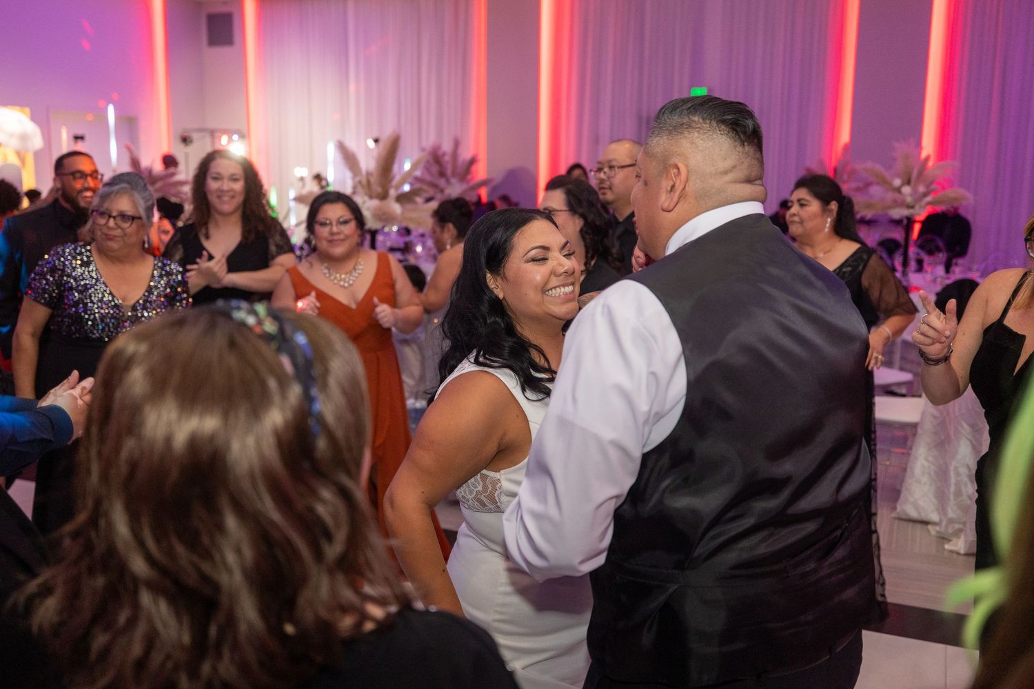 Dancing couples celebrate on a colorfully lit dance floor at an evening wedding reception.