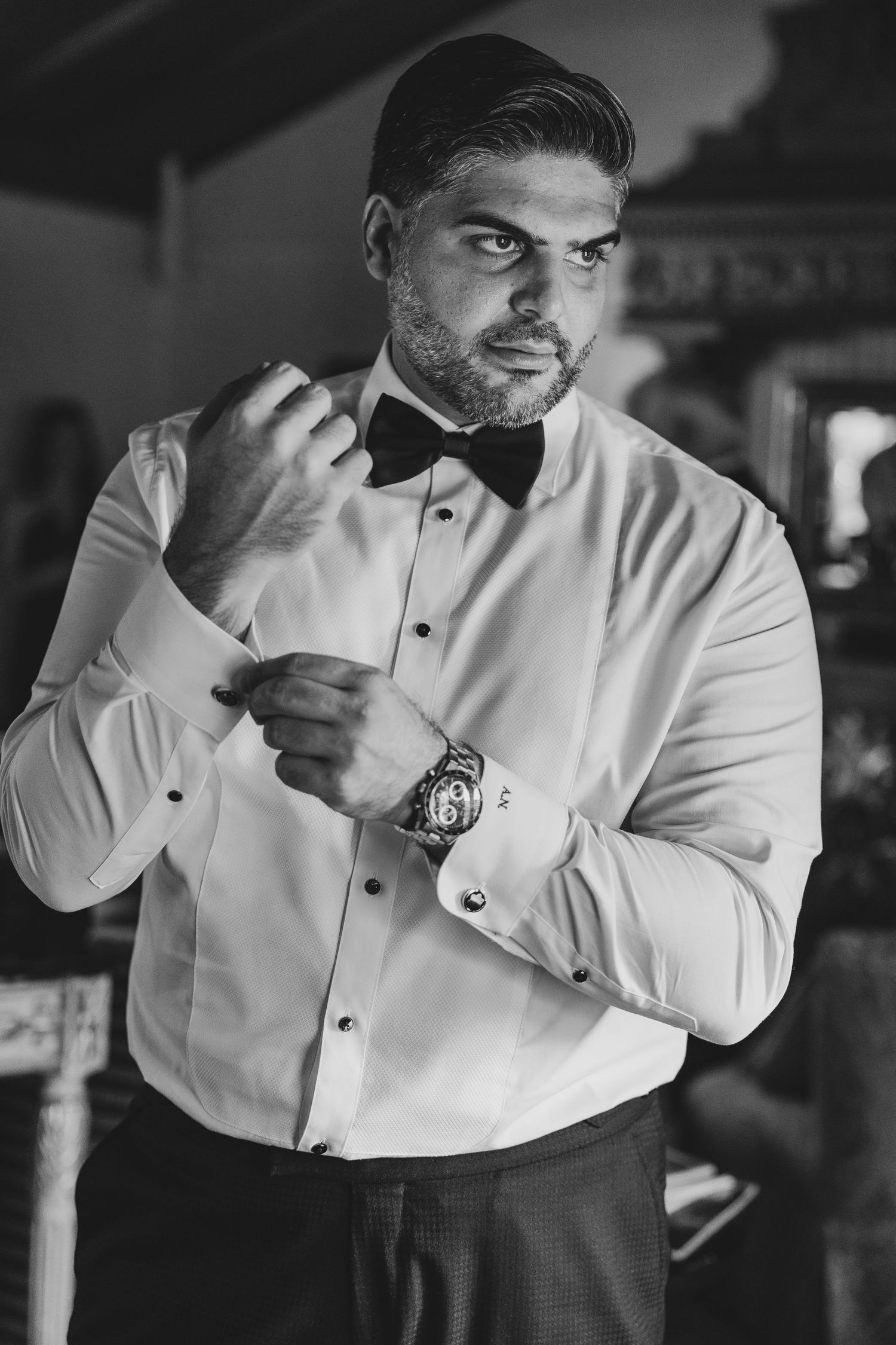 Groom in formal white shirt and bow tie adjusting his cuffs.