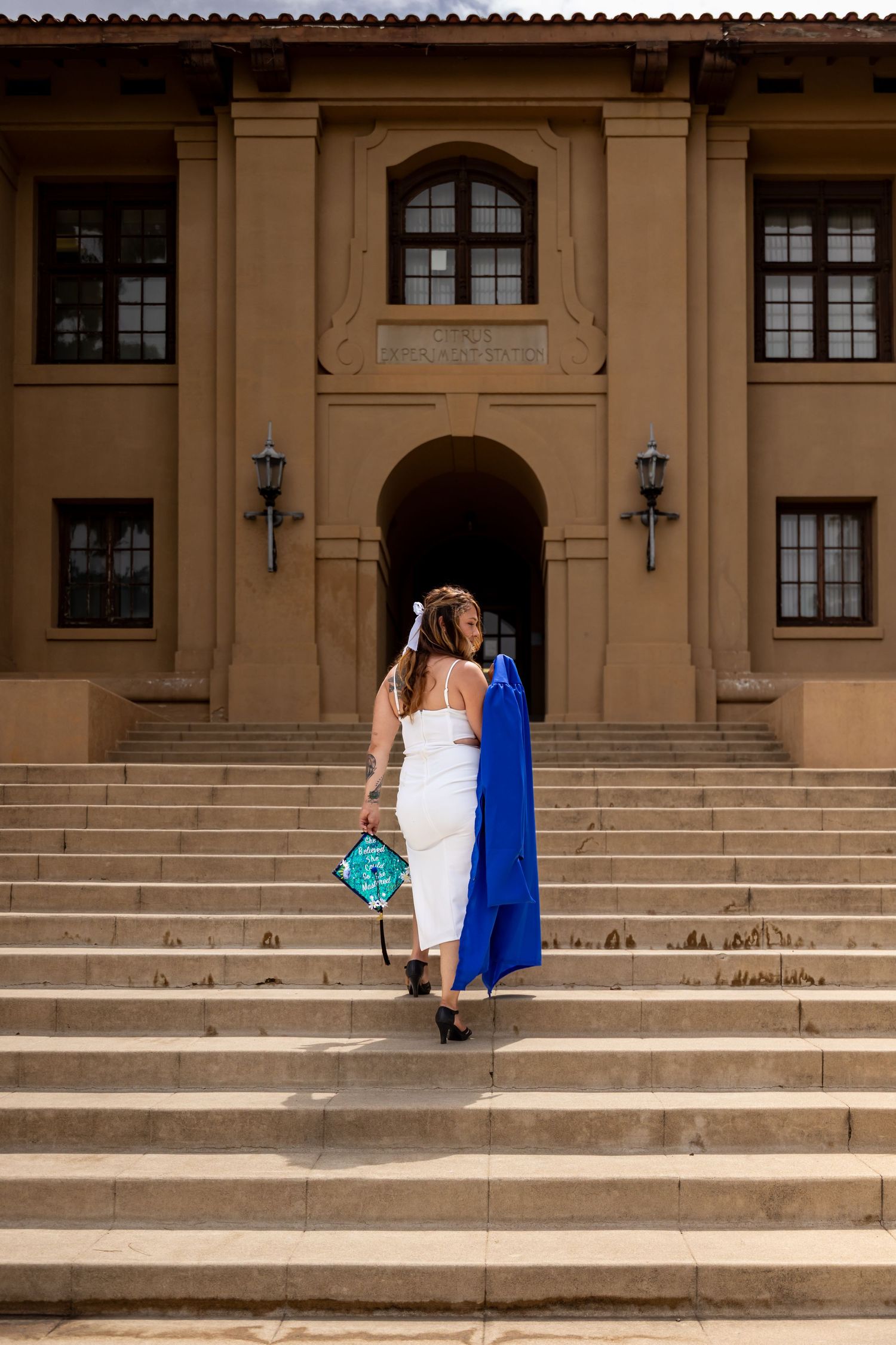 Two graduates ascending stone steps of historic building wearing white and blue graduation gowns.
