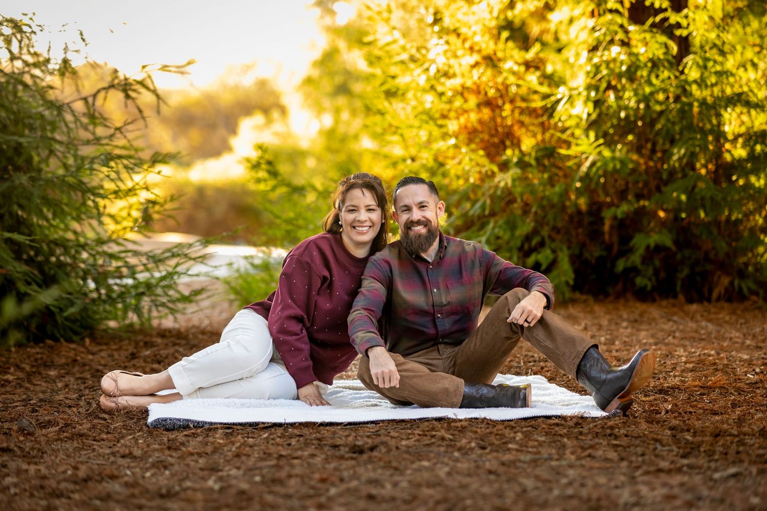Couple lying on blanket outdoors during golden hour with autumn foliage background.