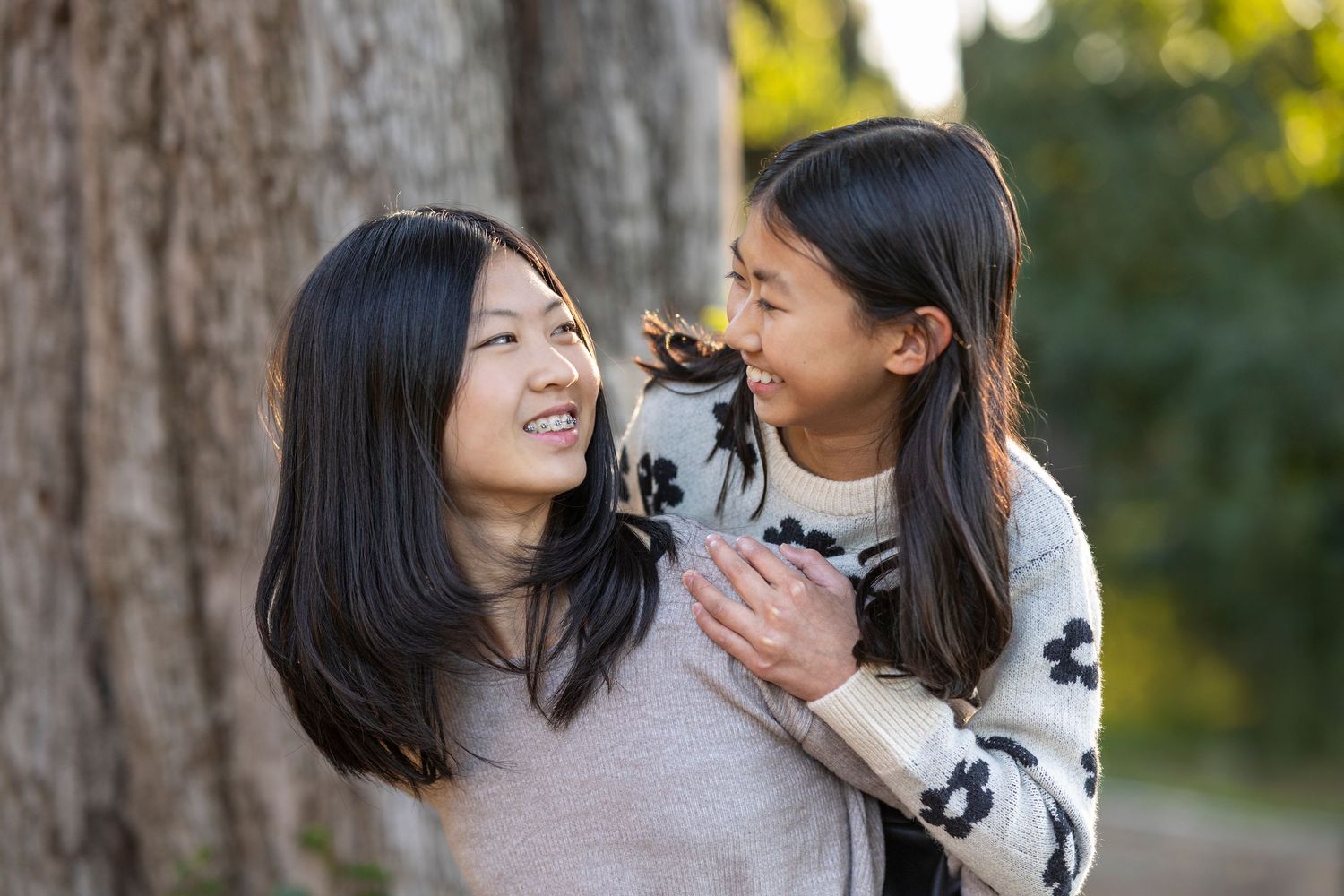 Two people share a joyful moment together while posing by tree trunk outdoors.