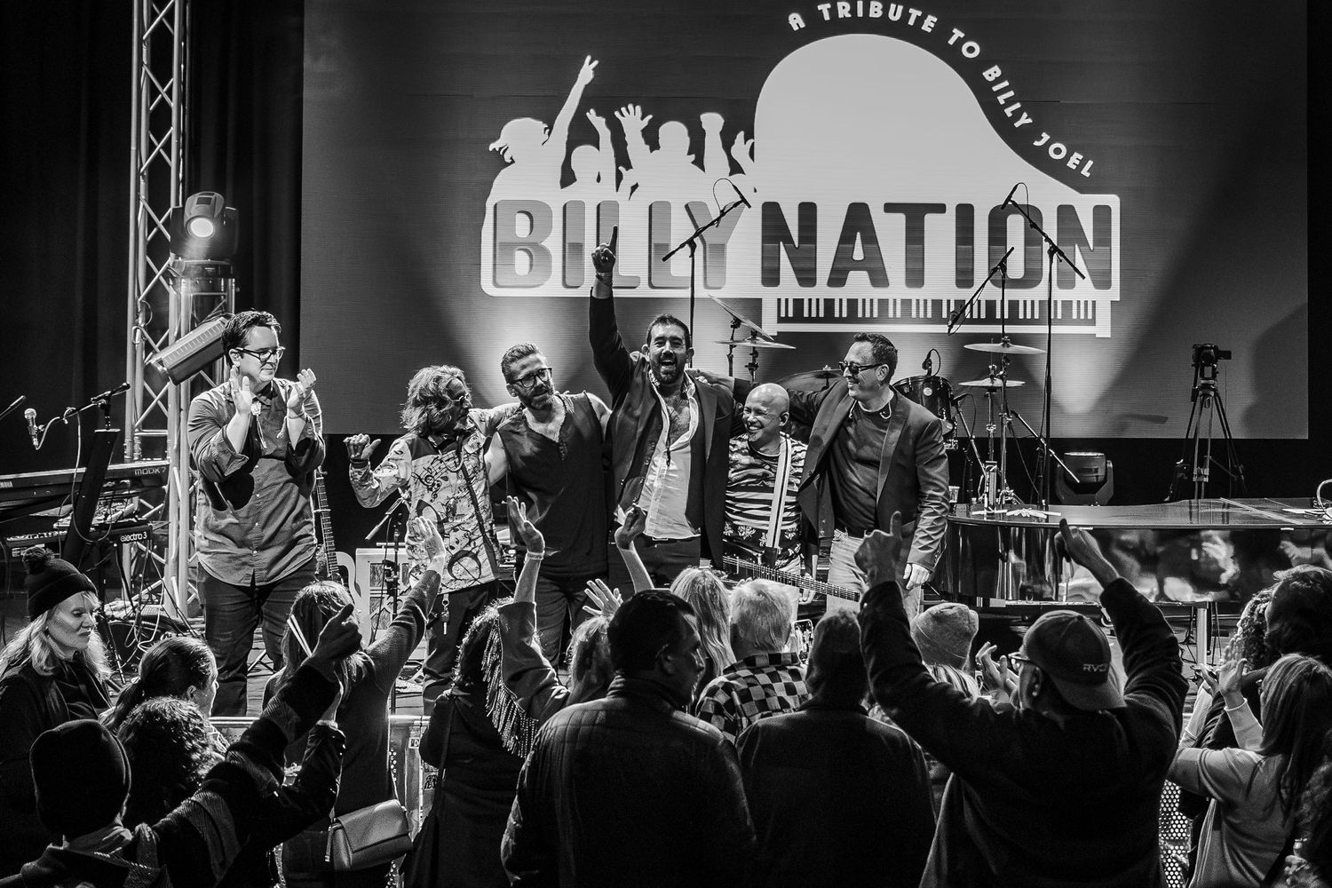 Concert performers and band members on stage at a Billy Nation tribute show with crowd silhouettes in foreground in Garden Grove.