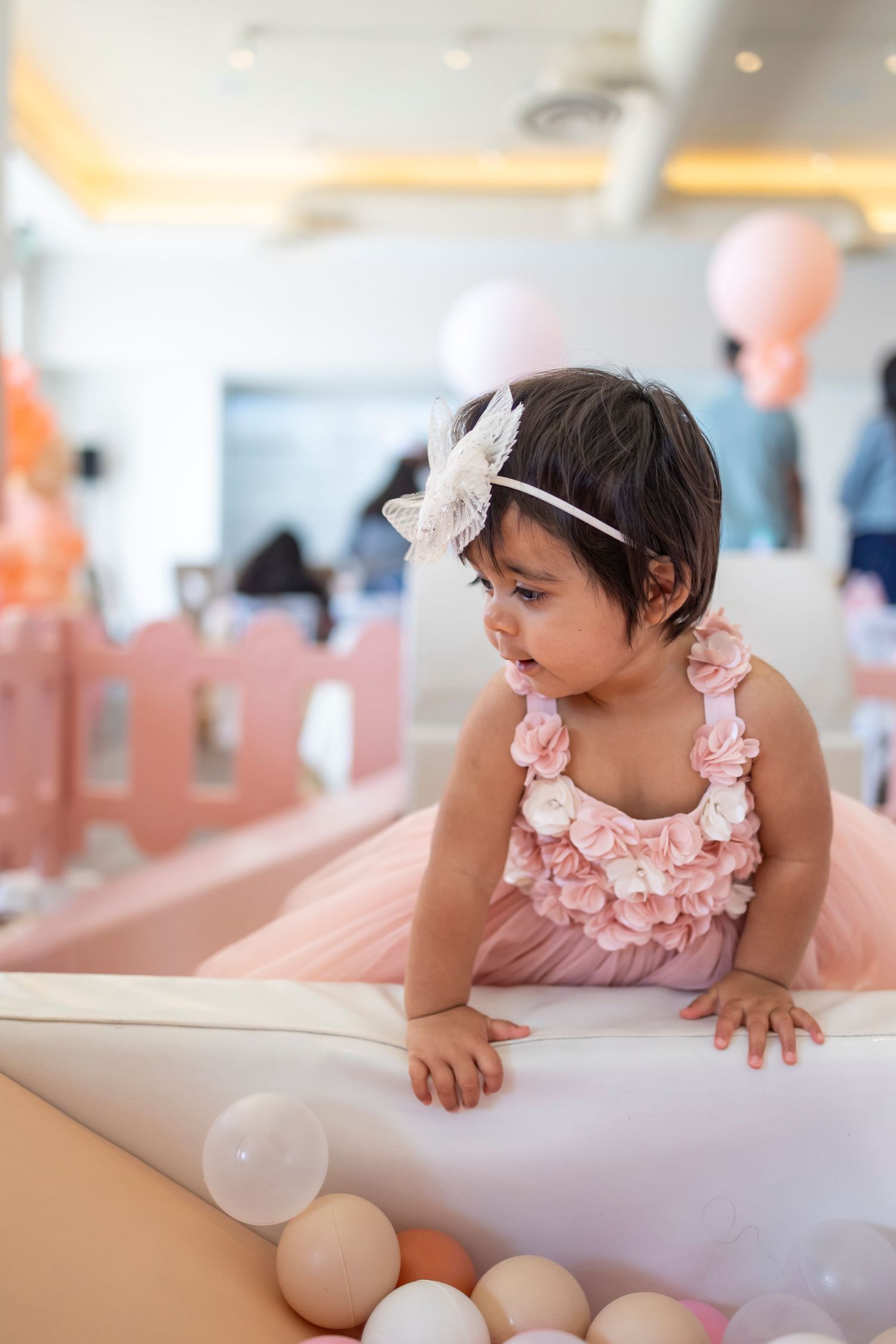Baby in pink ruffled outfit crawling on white furniture at a celebration in Huntington Beach.