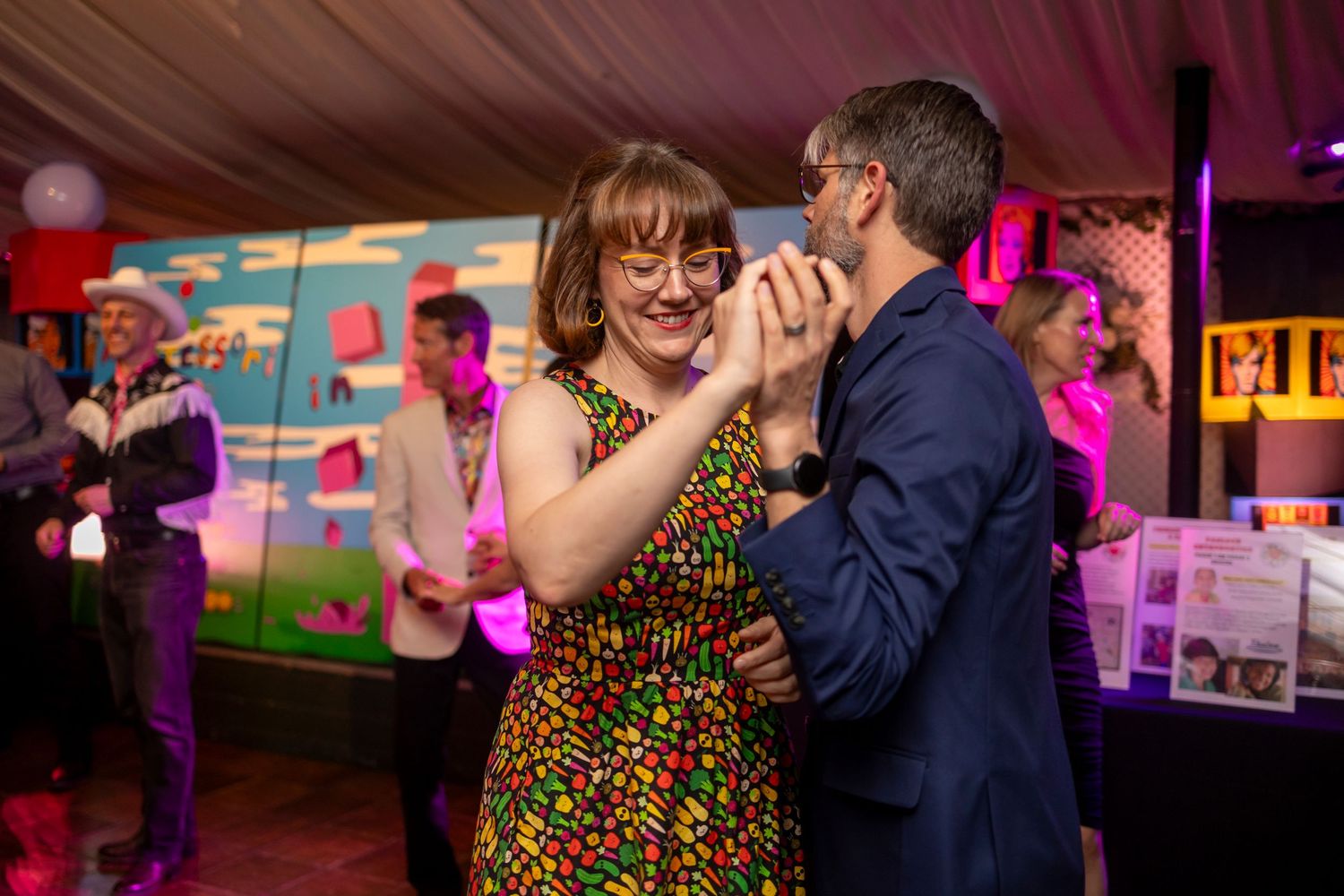 Couples dancing together at an indoor event with colorful lighting.