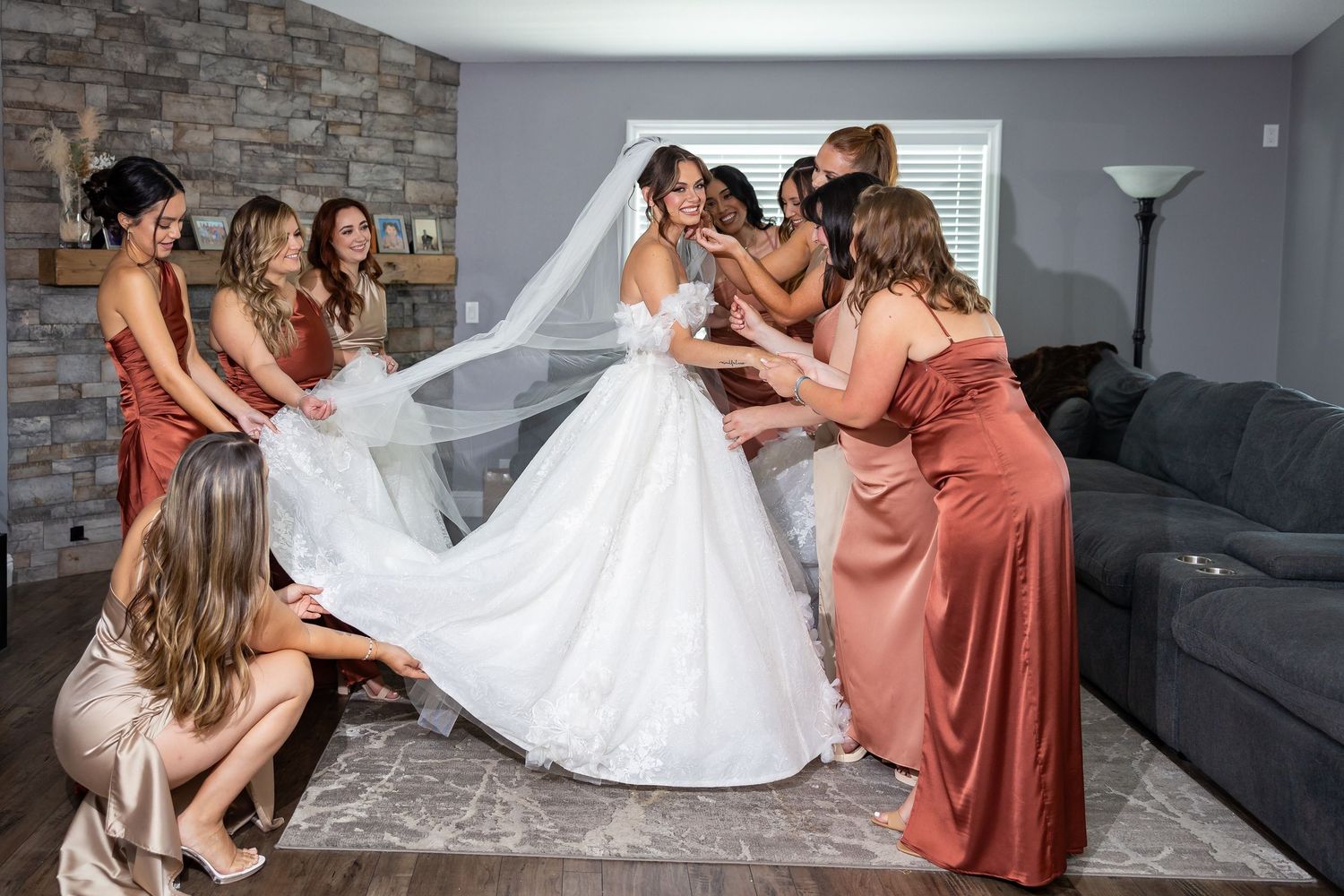 Bridesmaids in coral dresses help arrange the bride's wedding dress train in preparation.