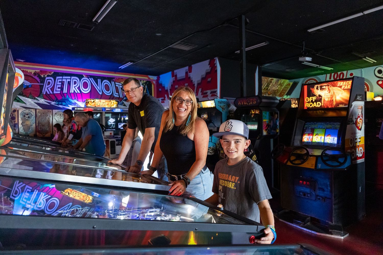 Group enjoying arcade games with colorful neon lights in background.