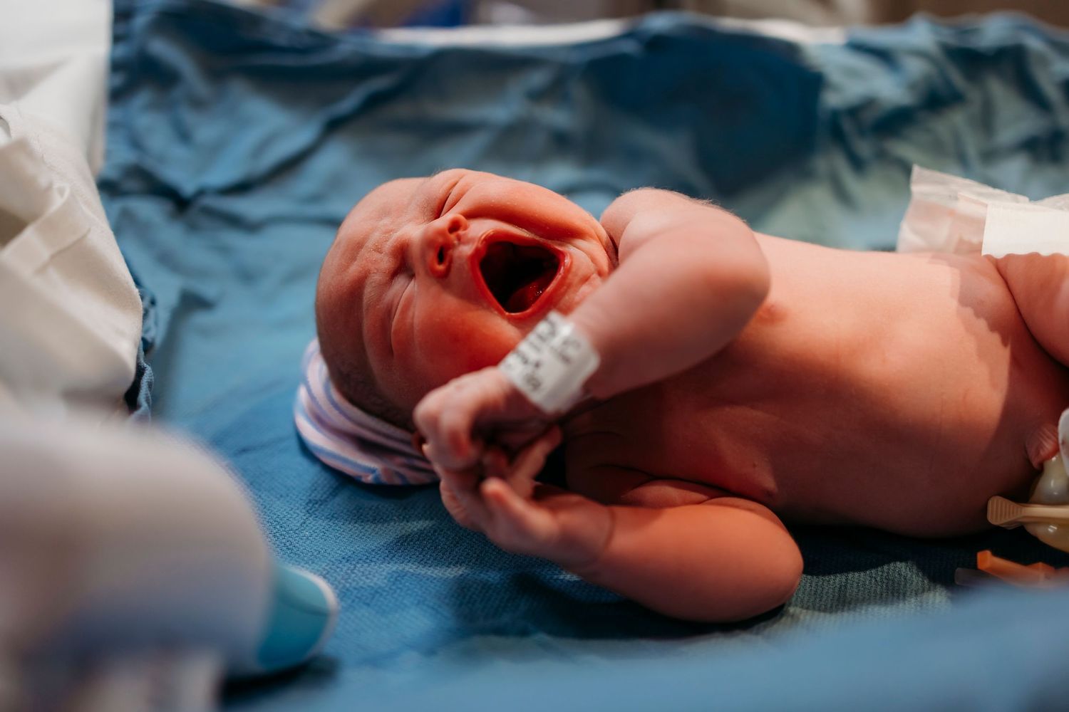 Newborn baby crying on blue hospital blanket during medical examination.