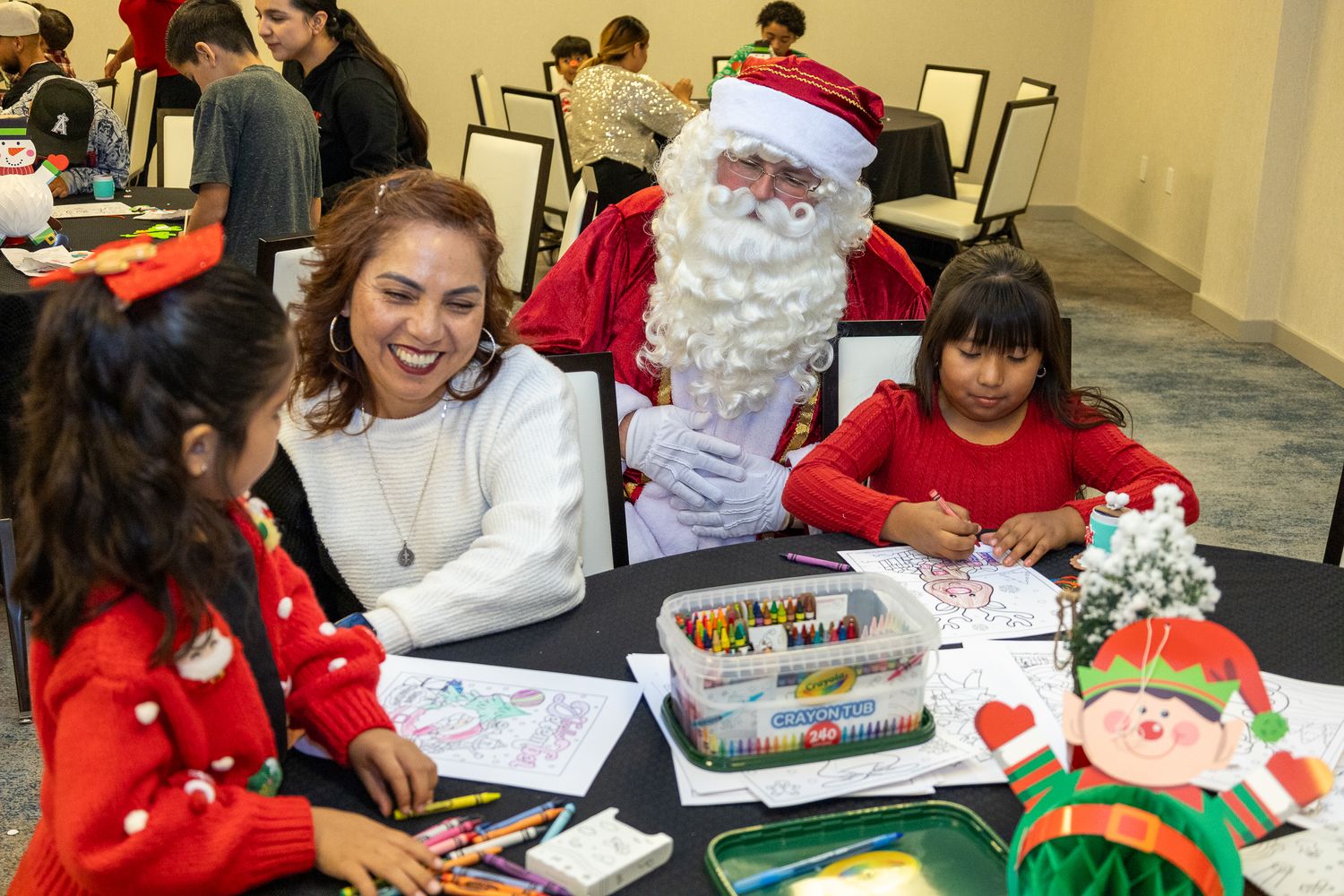 Students work on holiday crafts and activities while sitting at tables during a festive school celebration.