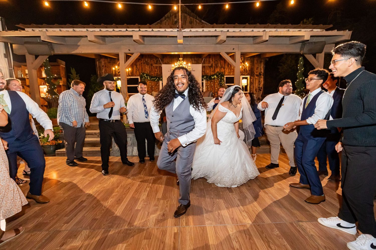 Wedding guests dance and celebrate together on a rustic wooden dance floor under strings of glowing lights in Oak Glen.