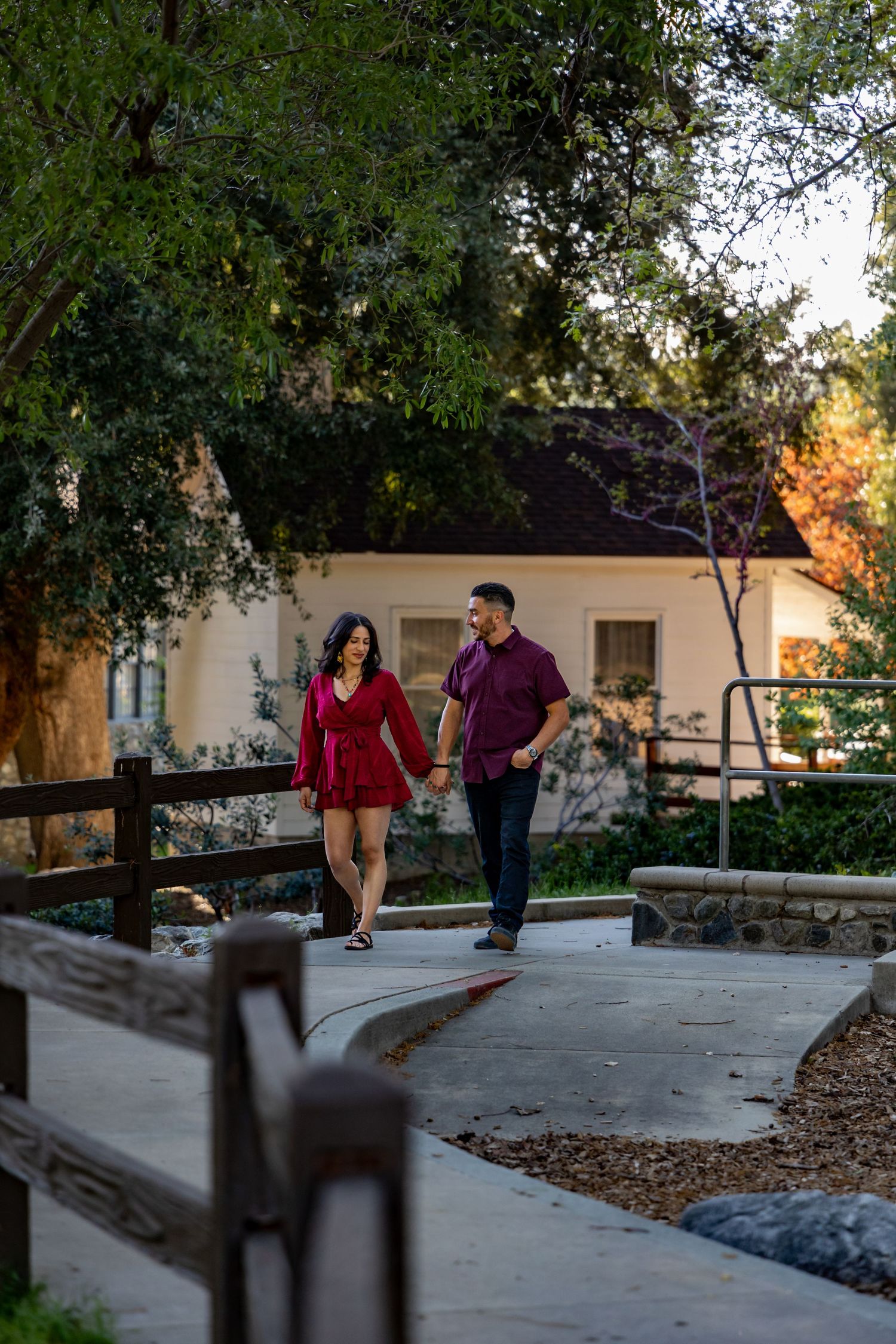 A couple in coordinating burgundy outfits walking along a curved pathway near a house.
