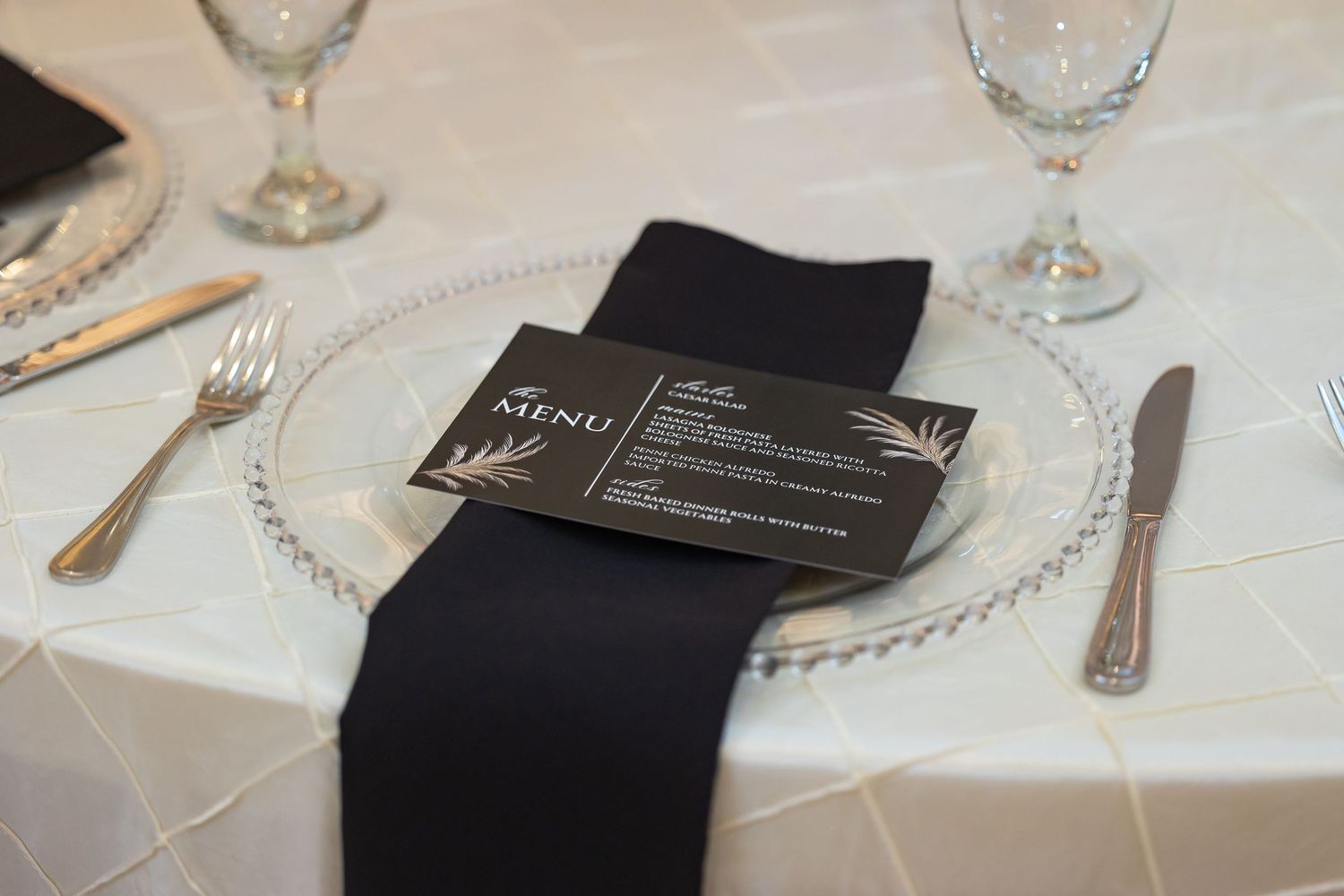Elegant place settings with crystal glasses and black napkins on white tablecloths.