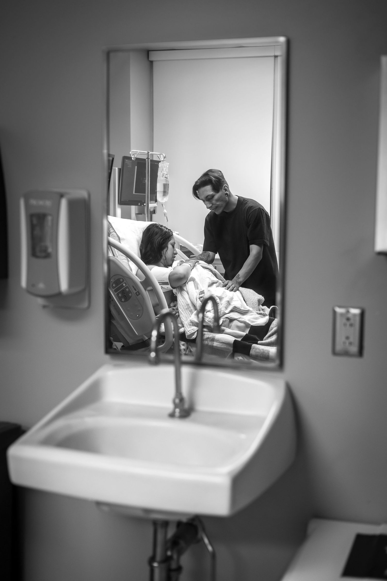 Black and white hospital room reflection in mirror showing medical staff caring for patient.