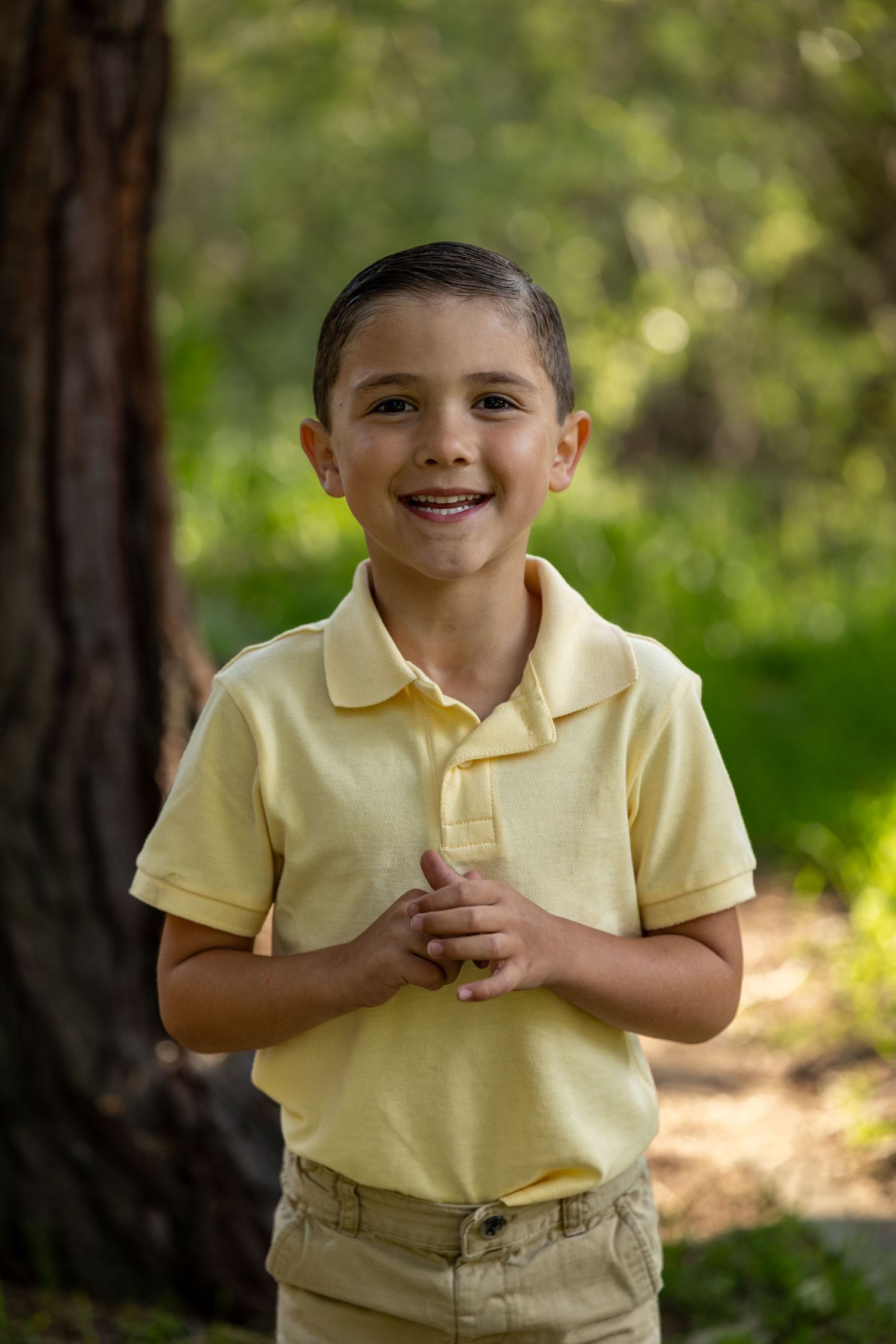 A child in a yellow polo shirt smiles brightly during an outdoor portrait session.