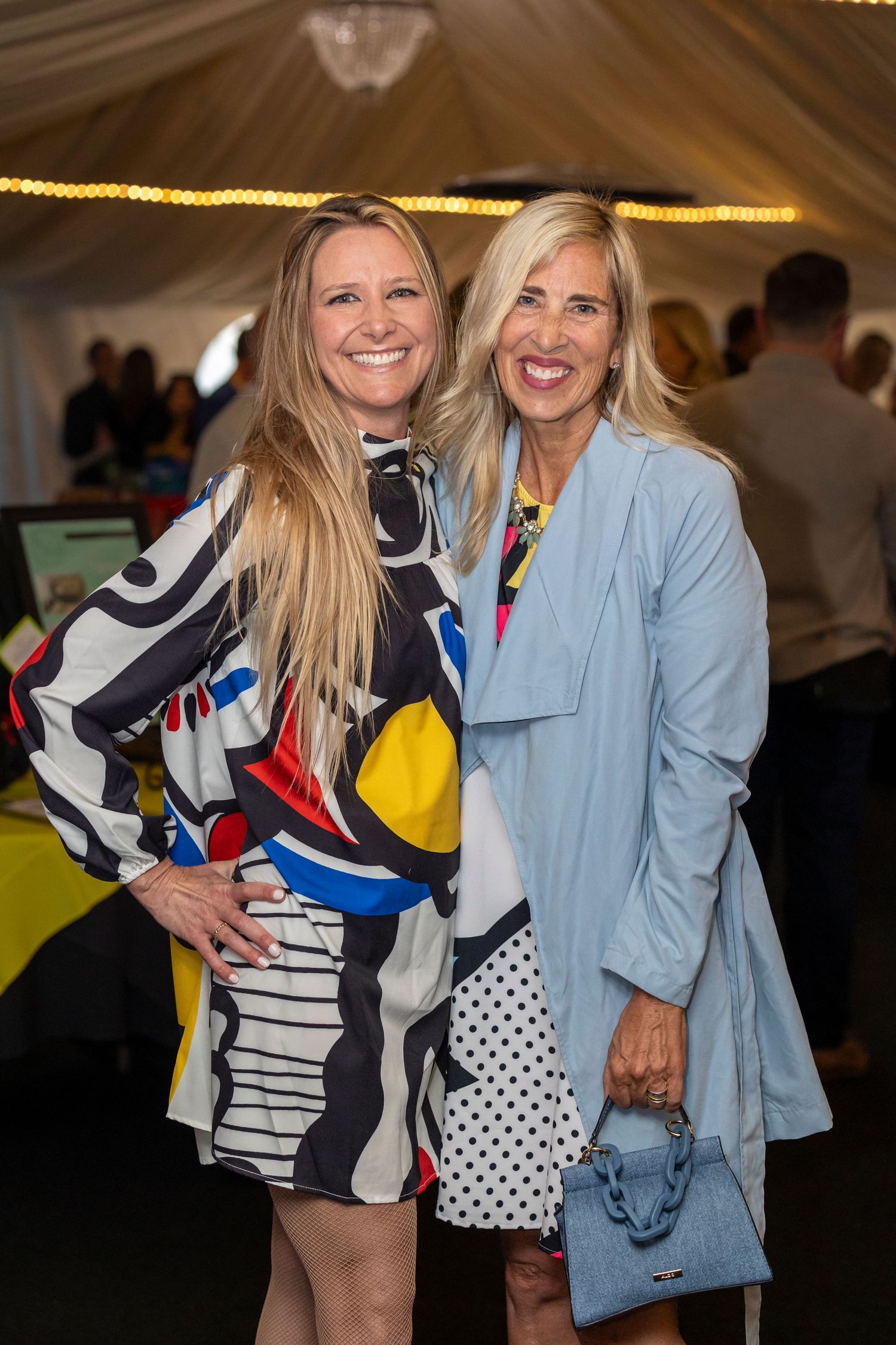 Event attendees in colorful patterned dresses posing together under tent lighting.