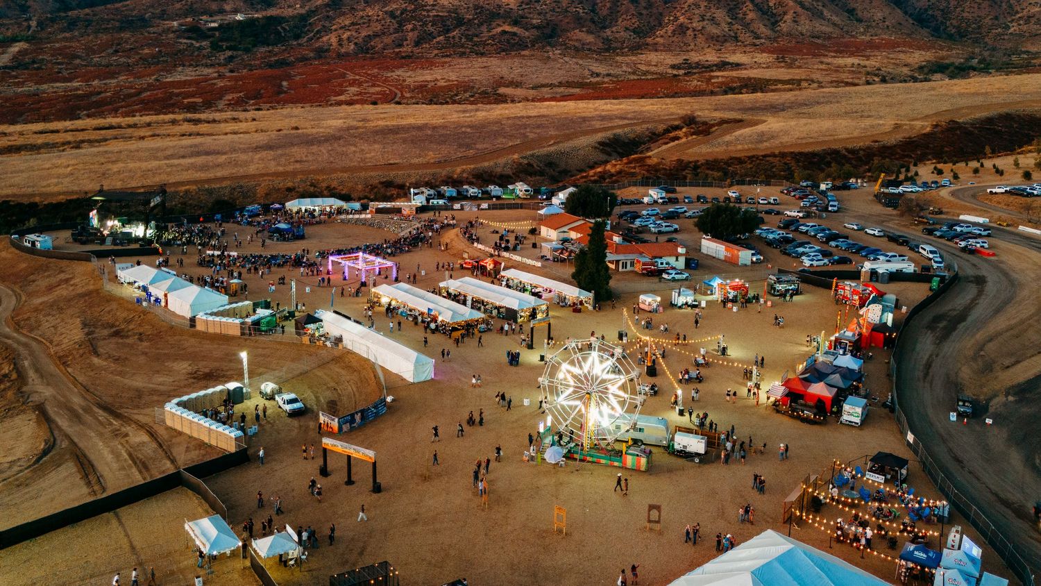 Aerial daytime view of festival grounds with temporary structures and gathering crowds.