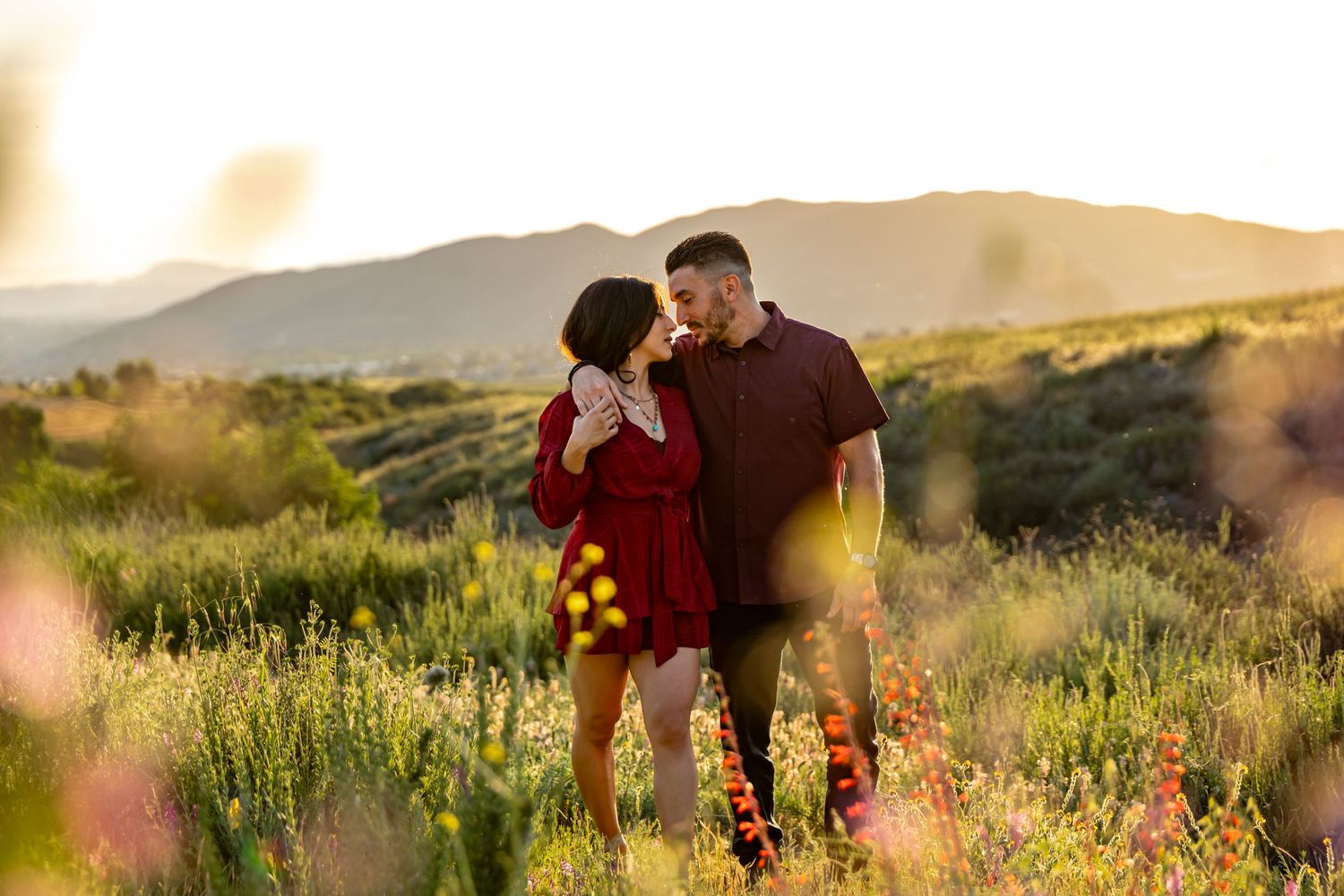 A couple embraces in a golden meadow at sunset with mountains in the background in Oak Glen.