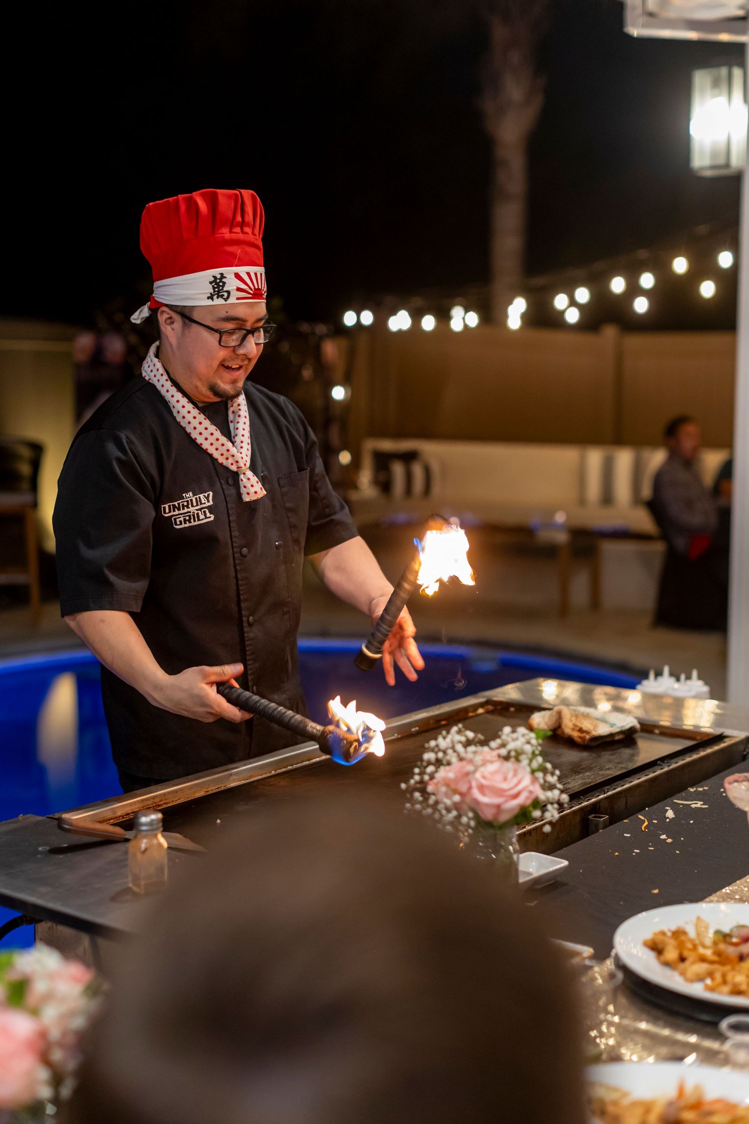 Chef performing hibachi cooking demonstration with flames at outdoor dinner event in Anaheim.