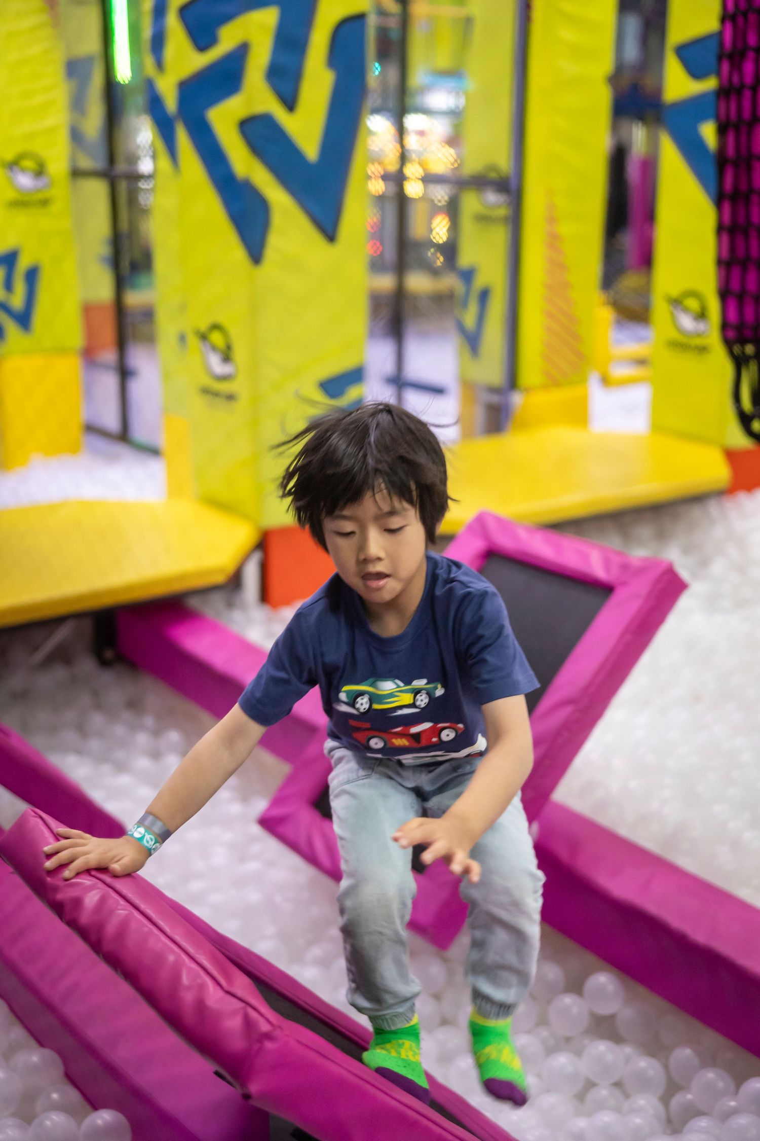Child playing and climbing on pink cushioned equipment in an indoor play area.
