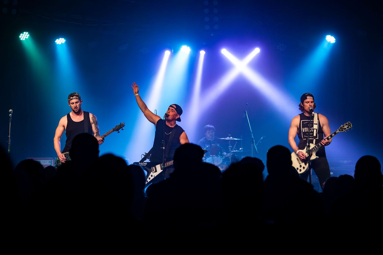 Three musicians perform on stage with dramatic blue spotlights and silhouetted crowd below in Pomona.