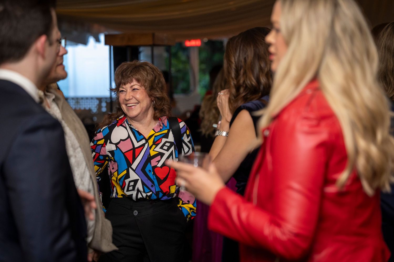 Group socializing at indoor event with person wearing colorful geometric pattern shirt.