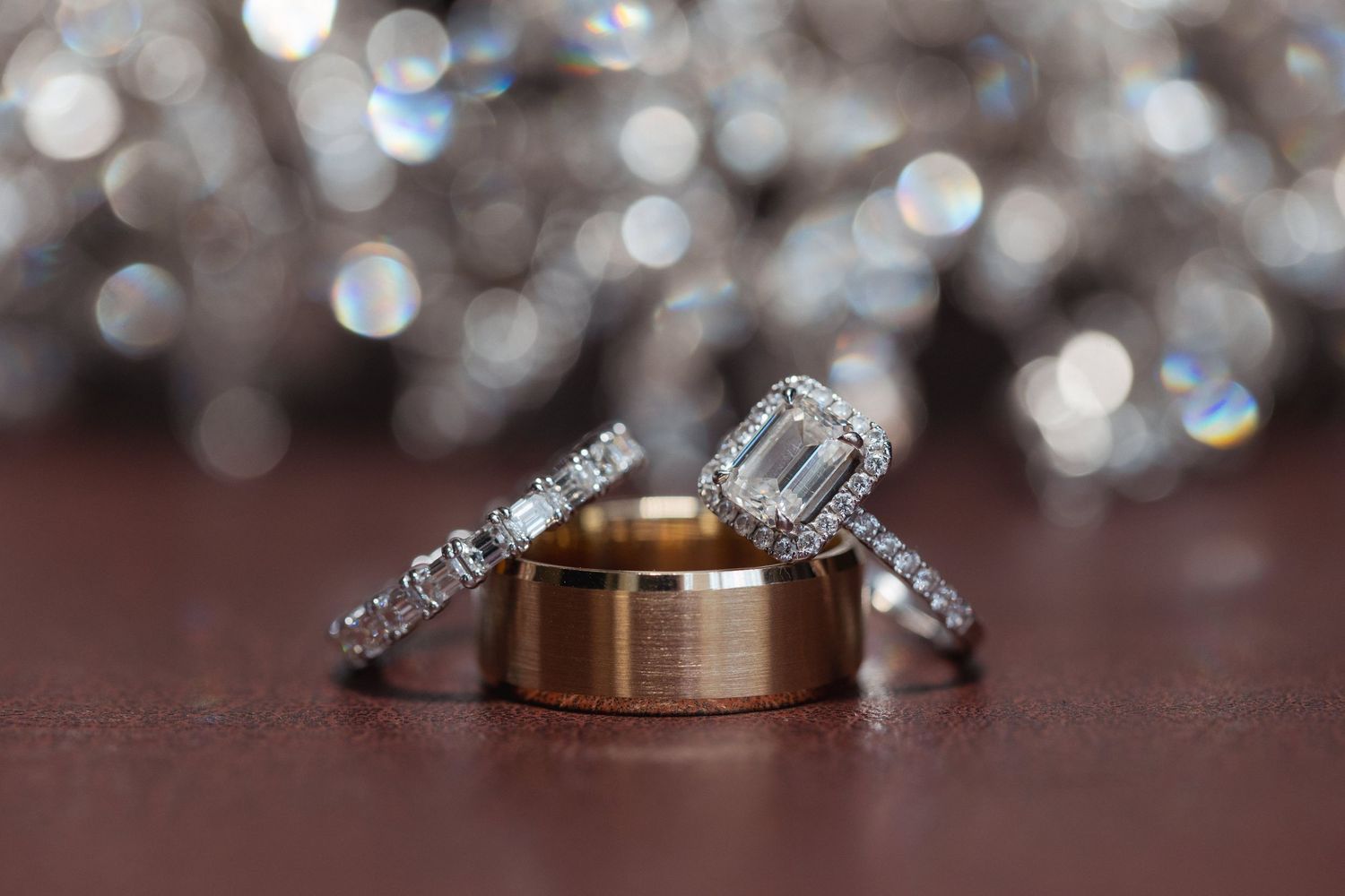 Wedding rings and diamond engagement ring arranged on dark surface with bokeh background.