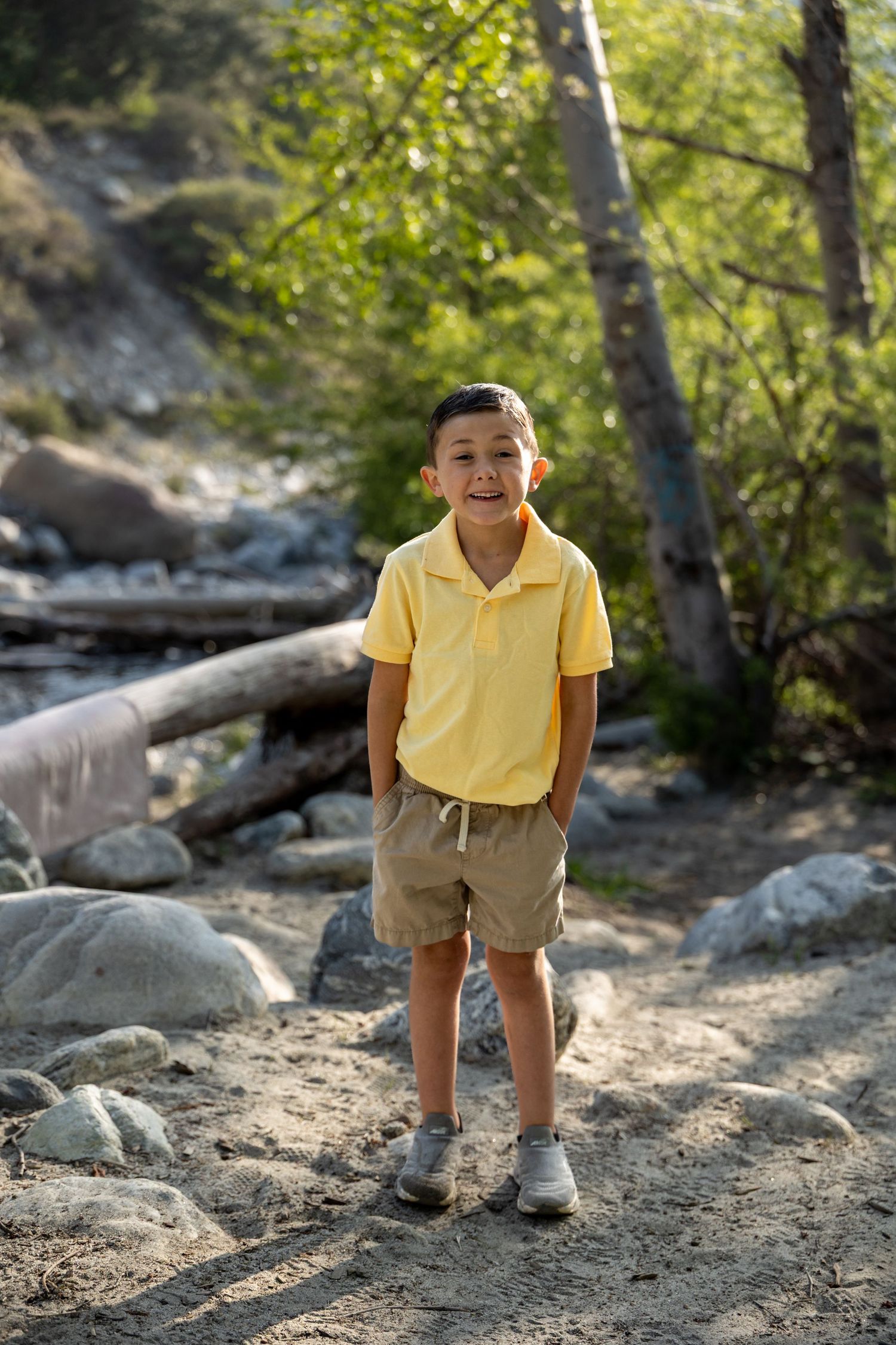 A child in a yellow polo and khaki shorts poses playfully on a rocky trail.