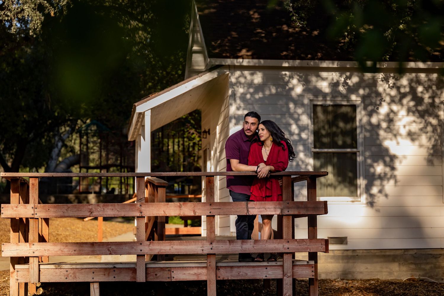 Couple embracing on a rustic wooden deck in front of a white chapel.