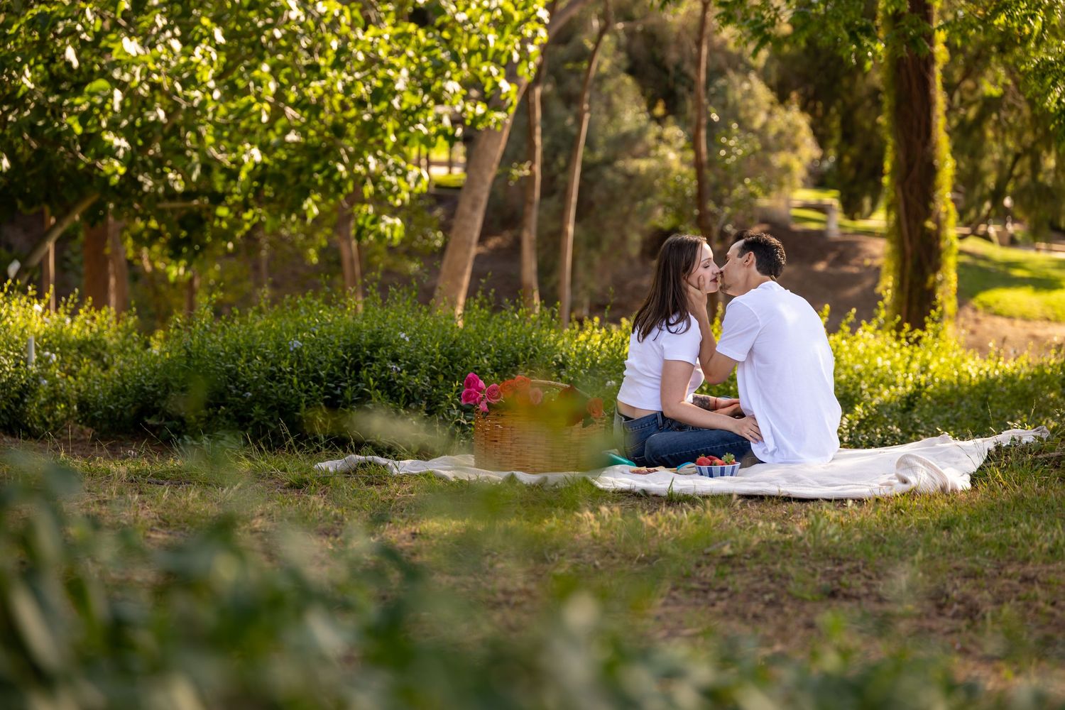 A couple enjoys a romantic picnic in a sunlit park setting.