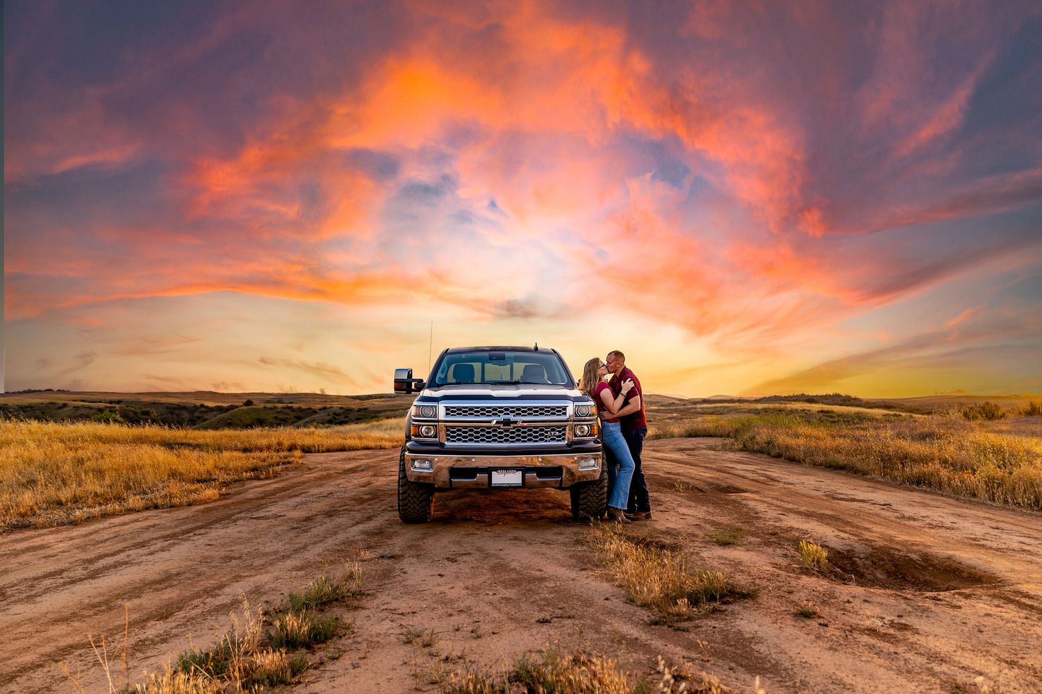 Dramatic sunset sky and truck parked on a rural dirt road with orange clouds in the background.