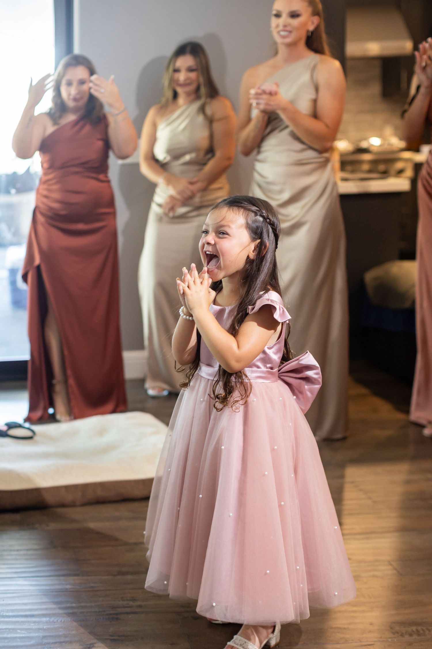 A joyful moment captured as bridesmaids watch a young girl in a pink dress express excitement.