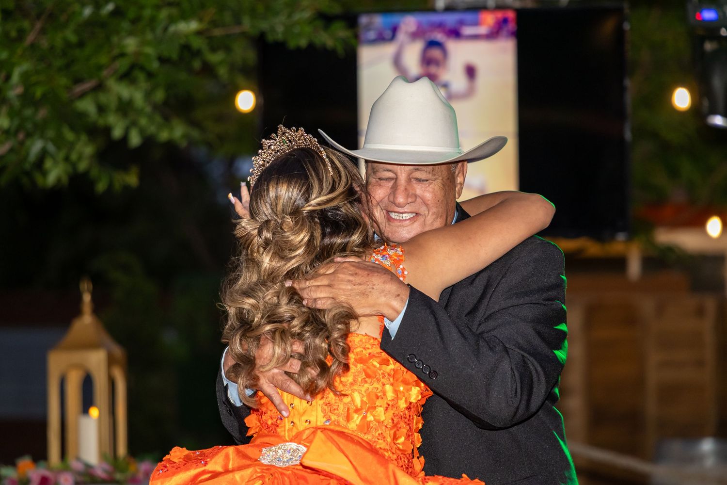 Person in cowboy hat dancing with someone in vibrant orange dress at an evening celebration.