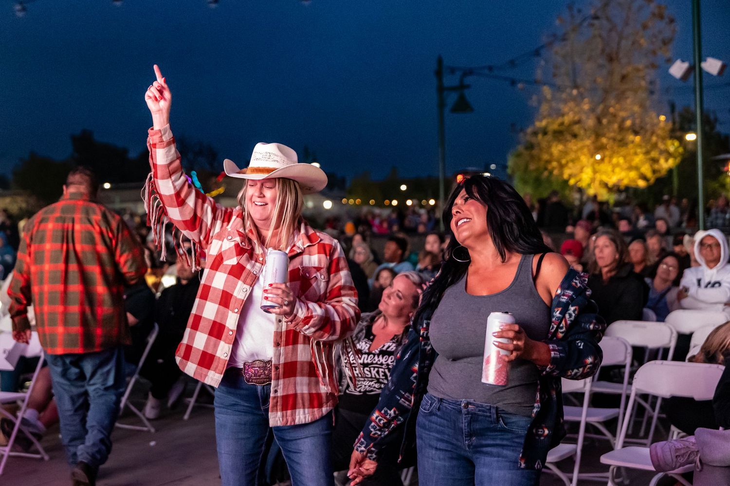 Crowd enjoying outdoor evening event with people in western attire dancing and celebrating.