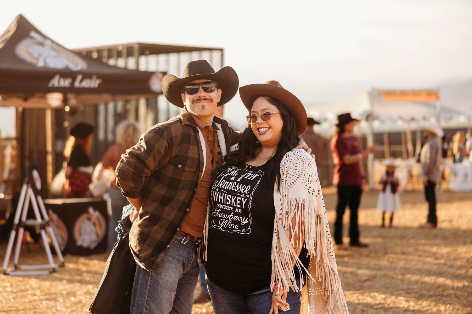 Group of friends enjoying drinks and conversation at an outdoor country music festival during sunset.