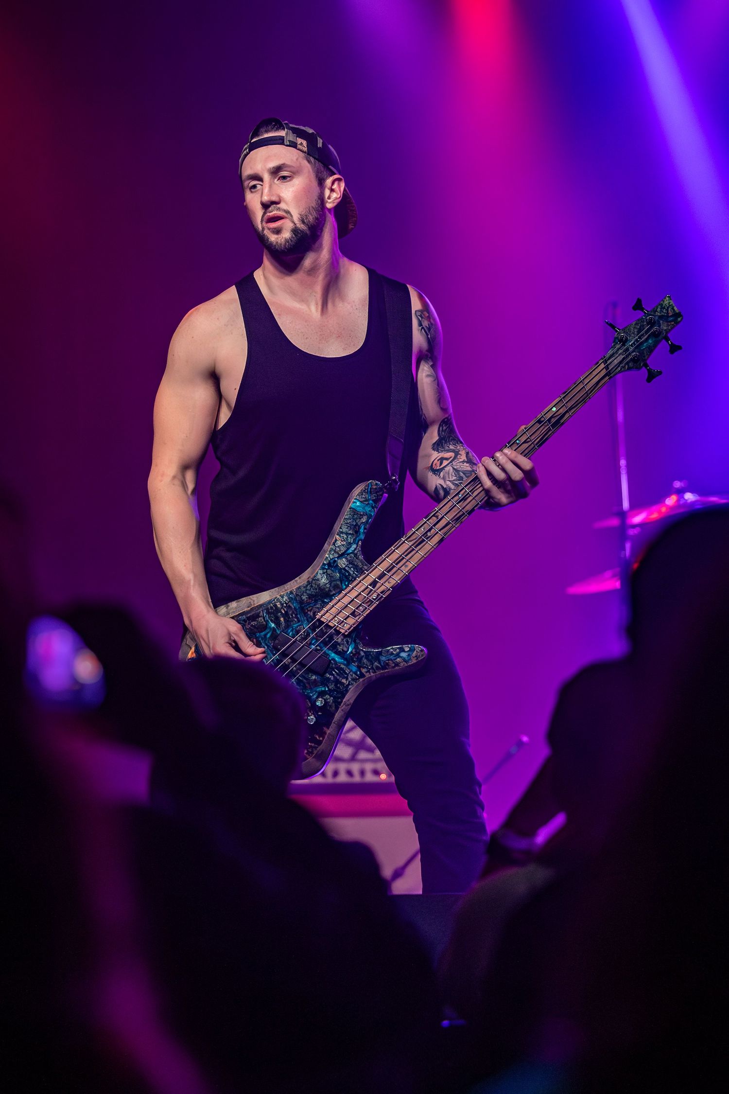 Bass player in black tank top performing with blue custom bass guitar under purple stage lighting in Pomona