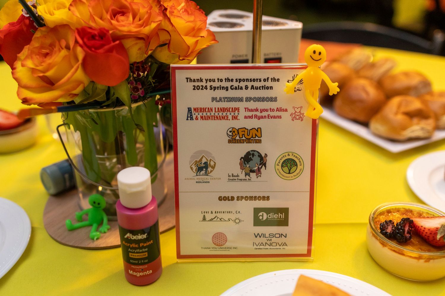 Colorful yellow table settings with small flower arrangements and place cards at an event.