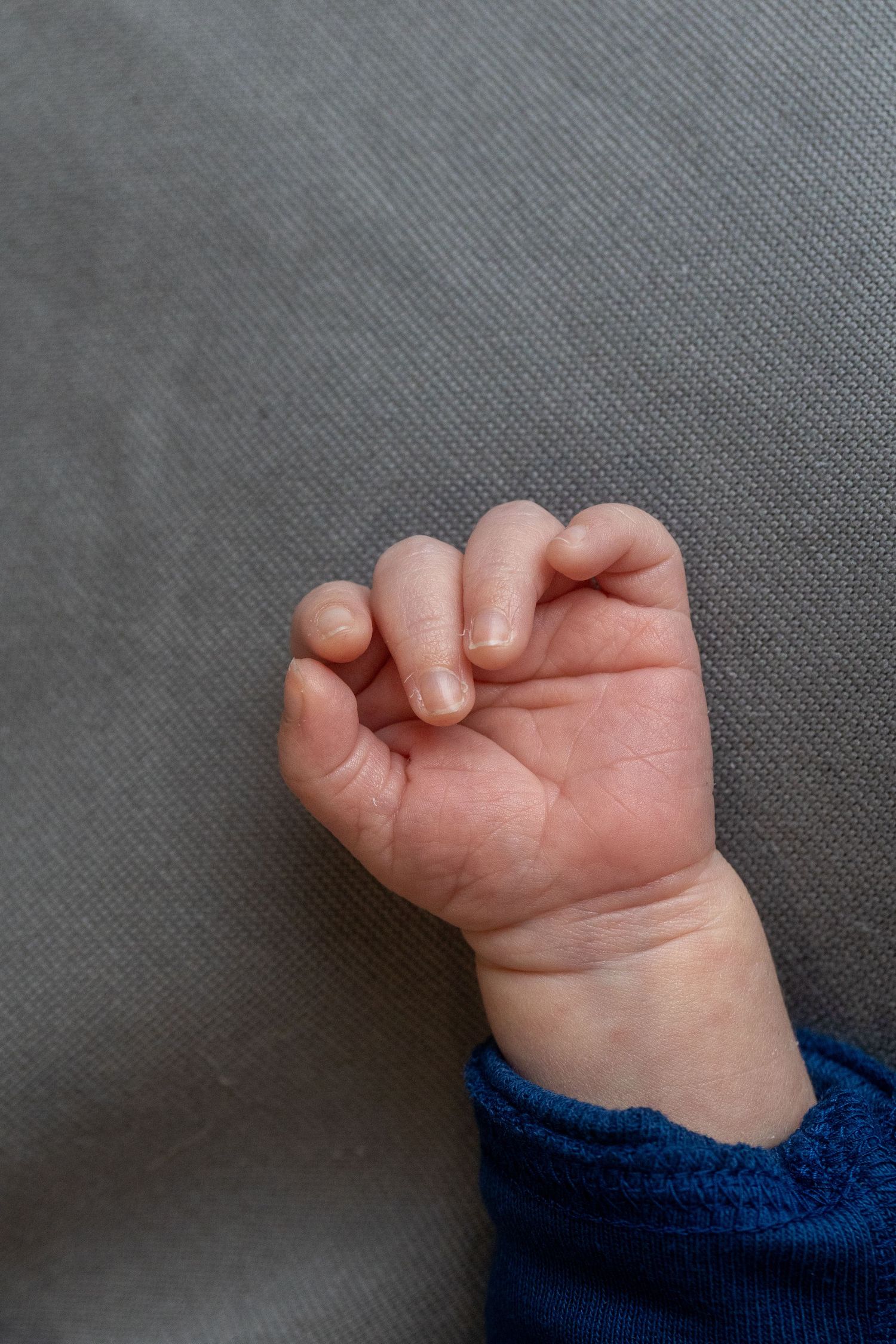 Close-up sequence of a baby's small hand and fingers against grey fabric.