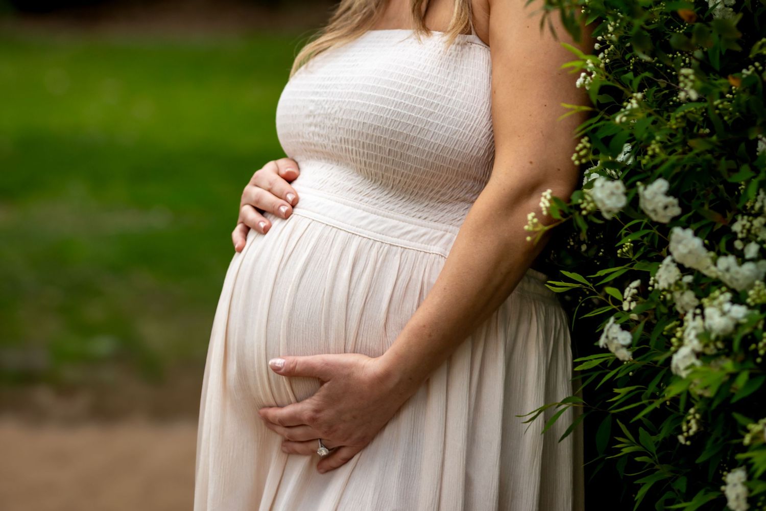 Close-up of a flowing white maternity dress against garden greenery.
