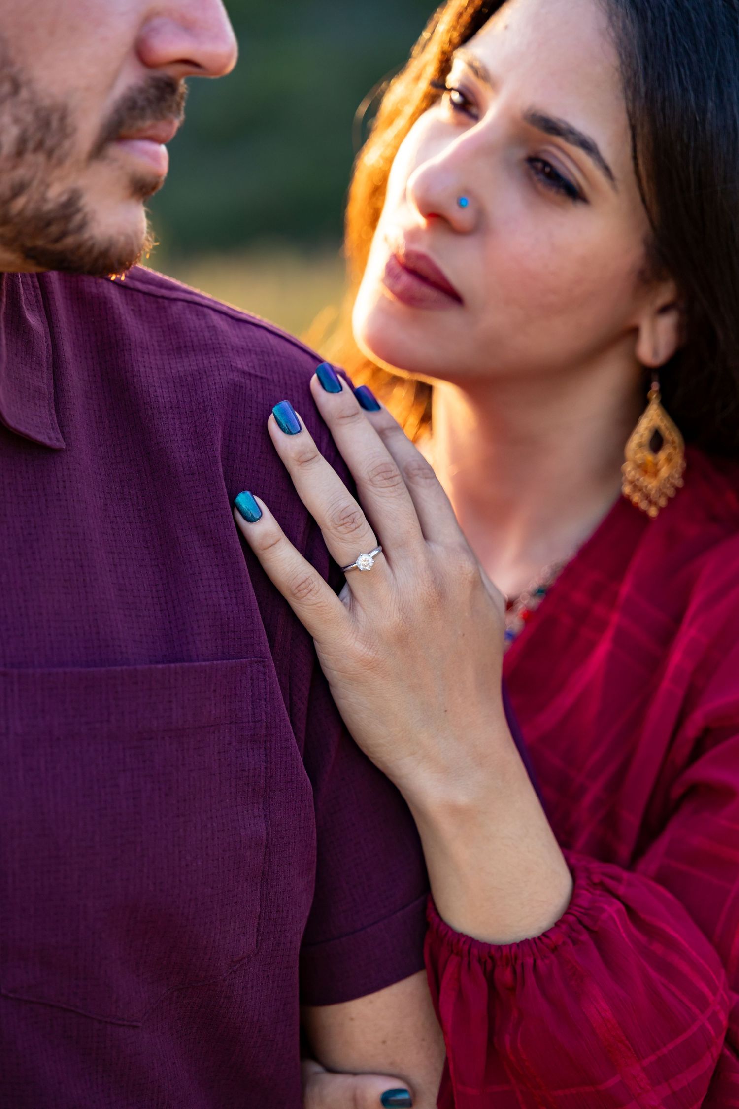 Close-up of engagement ring and turquoise nails against purple shirt in warm sunlight.