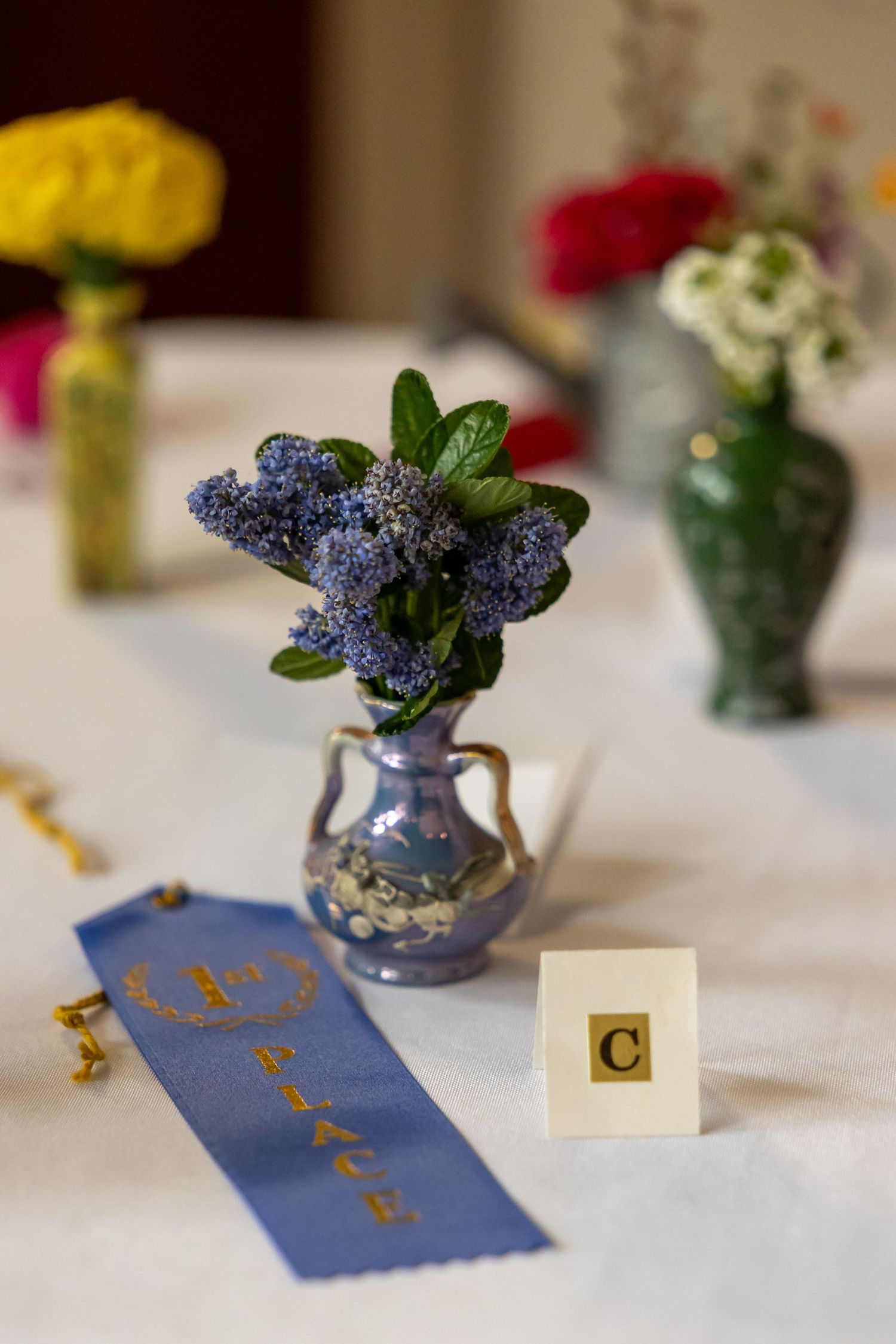 Small blue vases with purple flowers sit on a table with table cards and decorative elements.