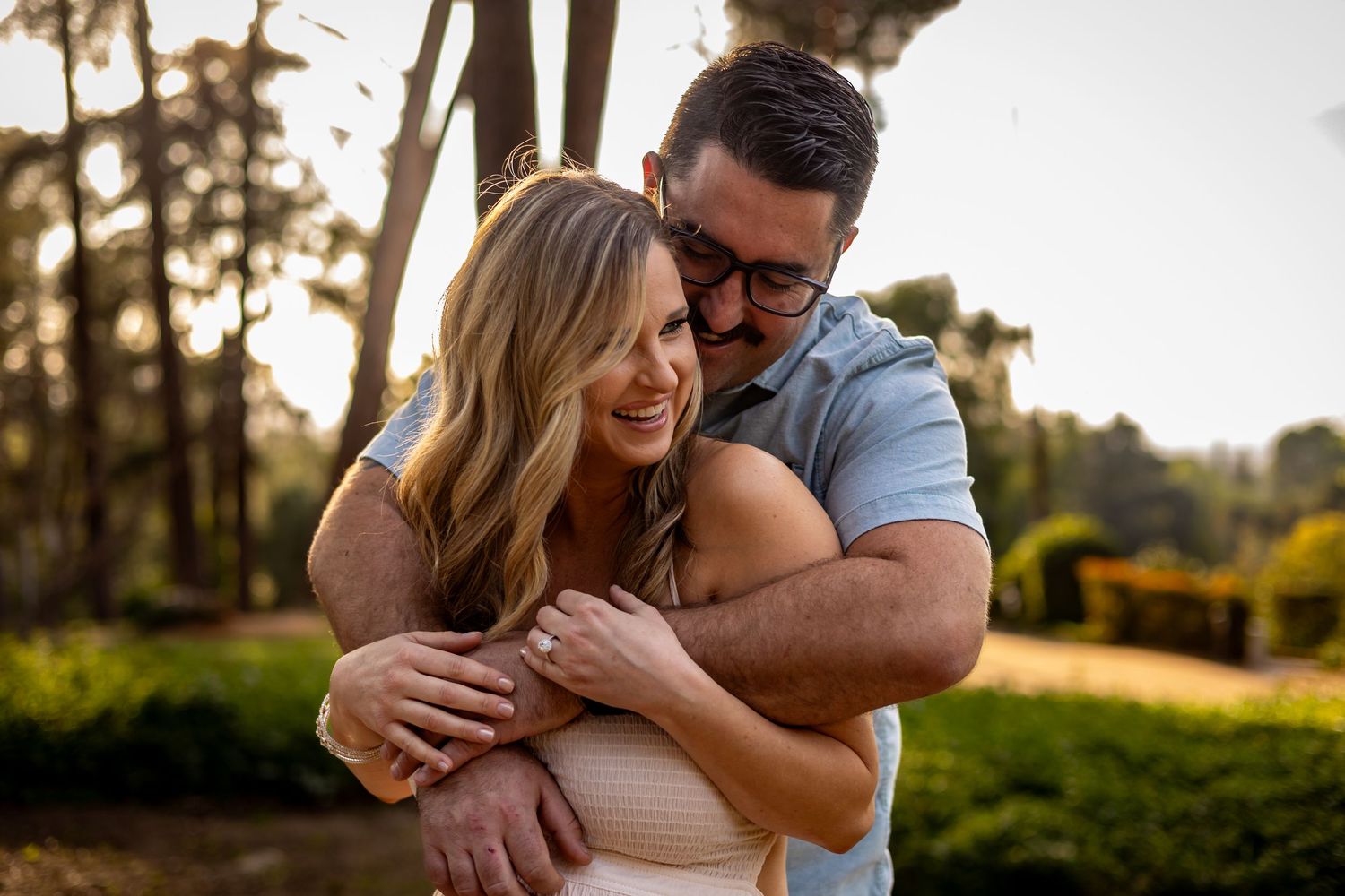 Joyful couple embracing during outdoor engagement photo session in golden sunlight.