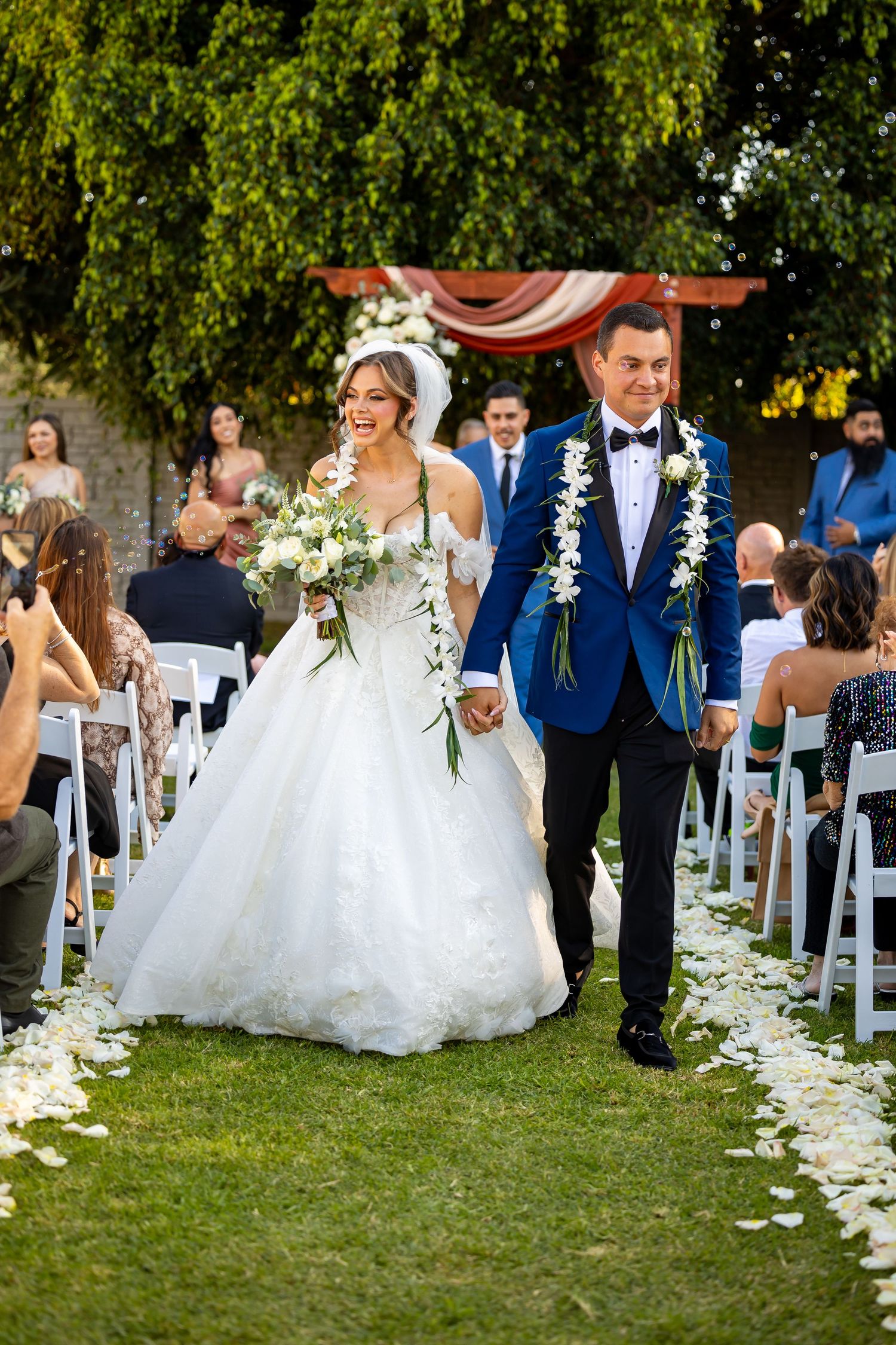 Outdoor wedding ceremony aisle decorated with white flower petals and folding chairs.