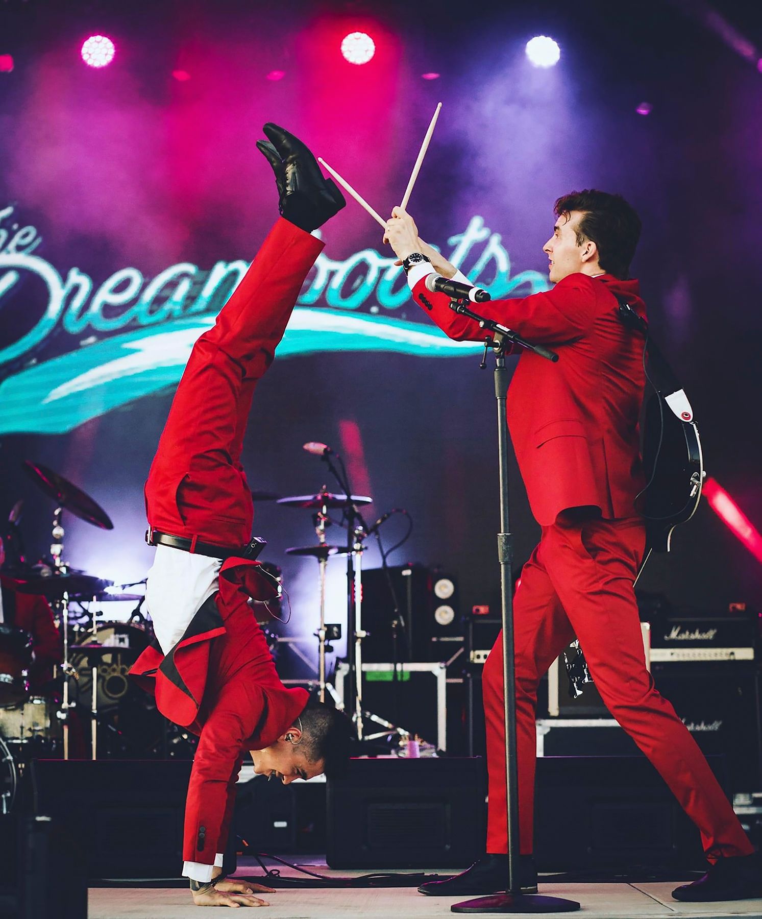 Two performers in red suits doing acrobatic moves on stage with colorful lighting and Dream logo backdrop.